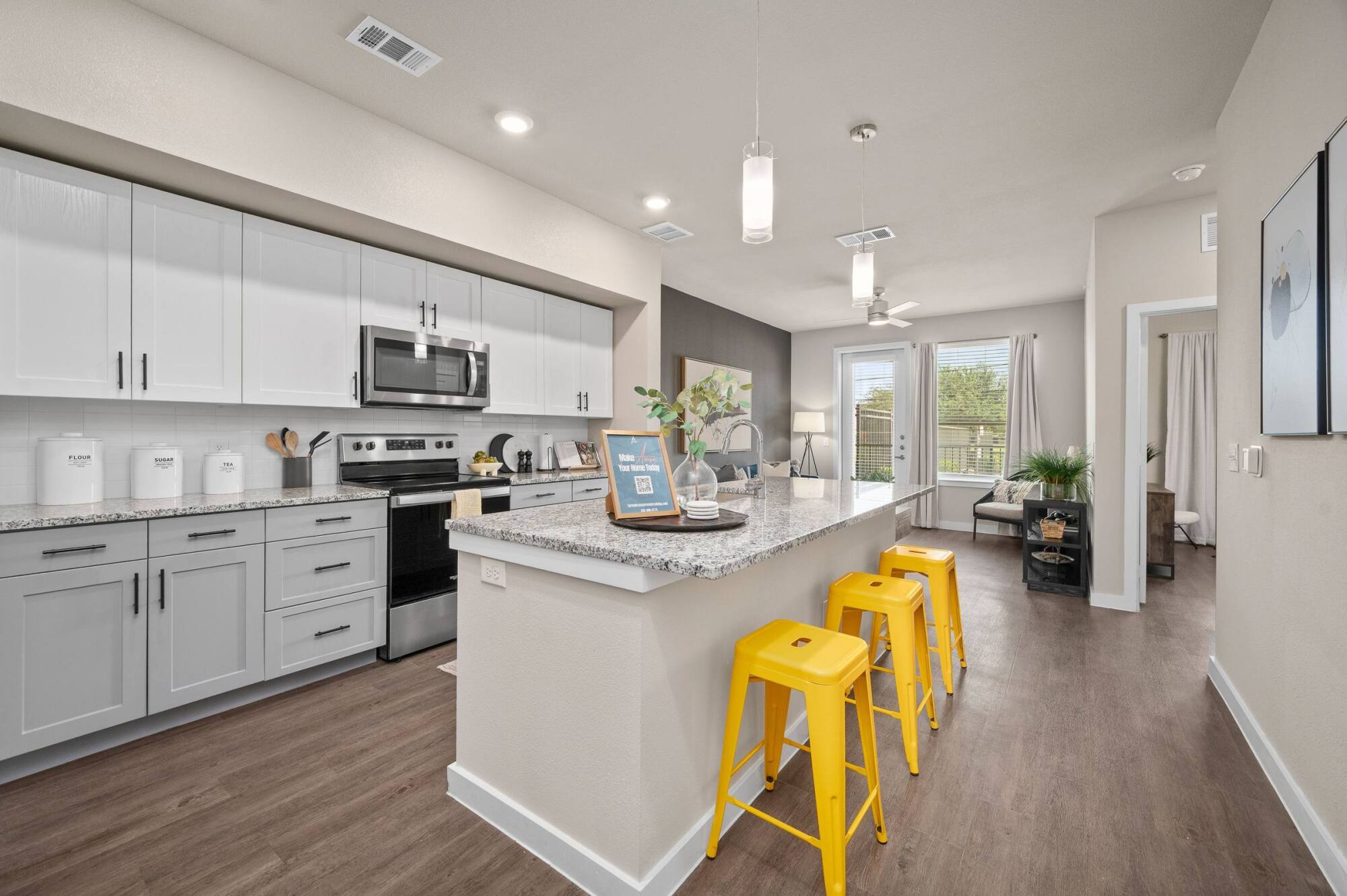 Modern kitchen with gray and white cabinets, granite island, and three bright yellow stools.