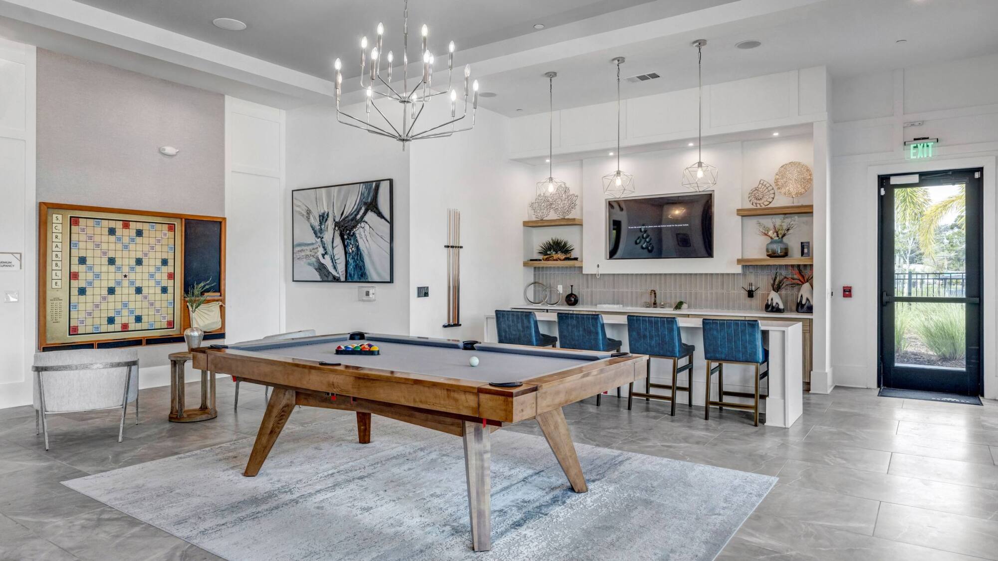 Modern game room with a pool table, bar seating, wall art, and a large Scrabble board on display.