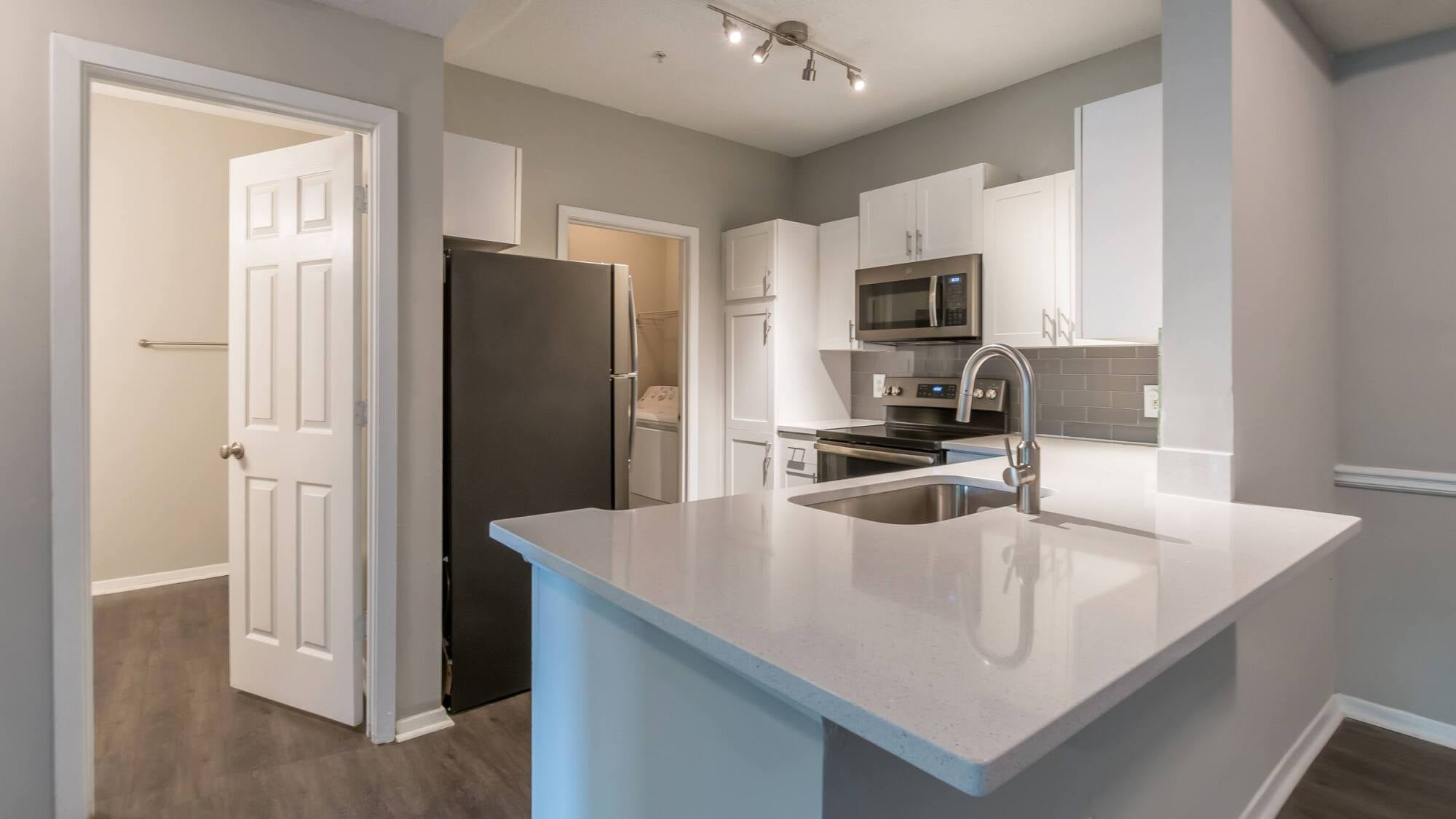 Modern kitchen with white cabinets, stainless steel appliances, and a sink with a curved faucet on an island.
