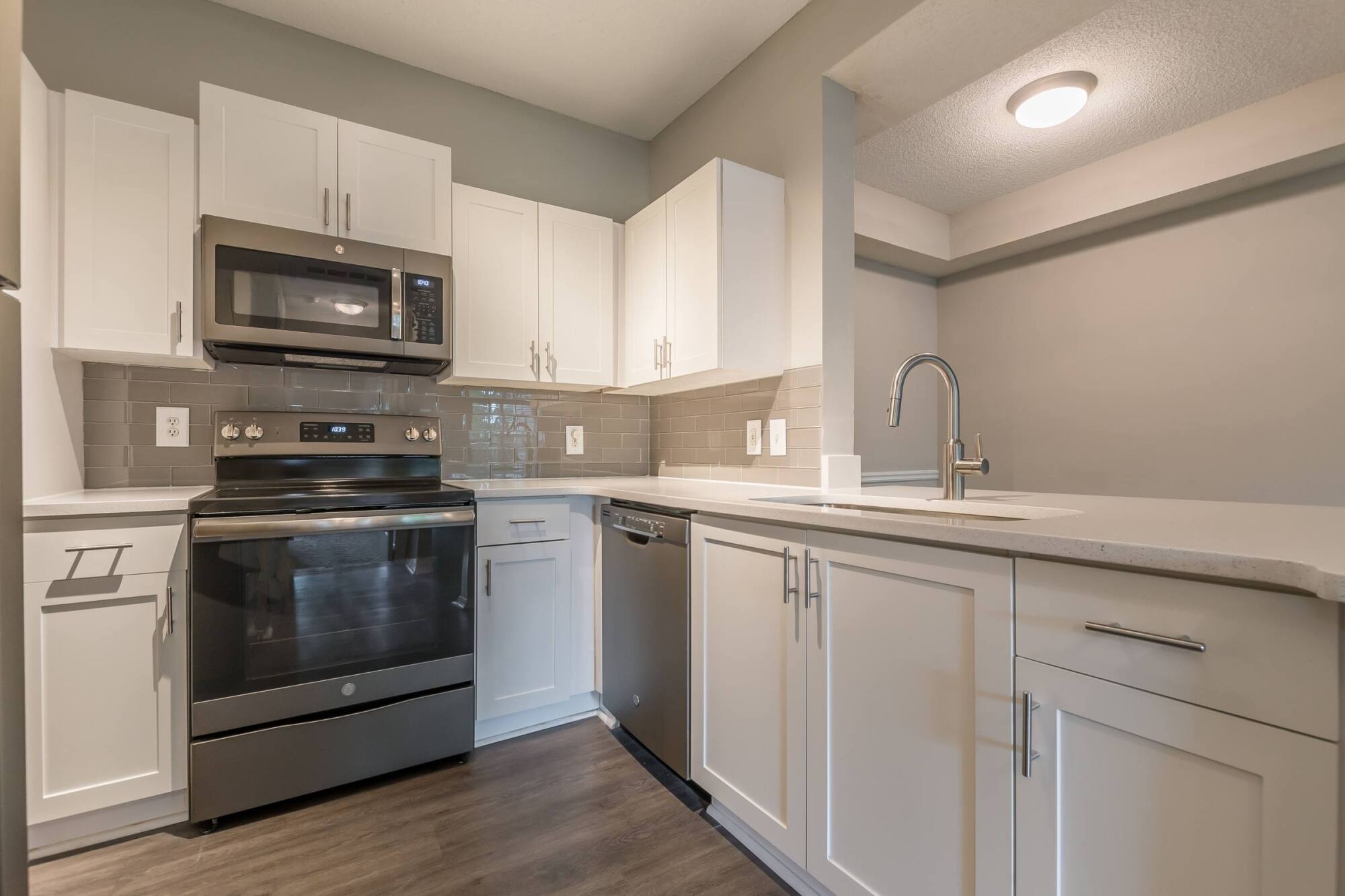 Modern kitchen with white cabinets, stainless steel appliances, and a sink with a curved faucet on an island.