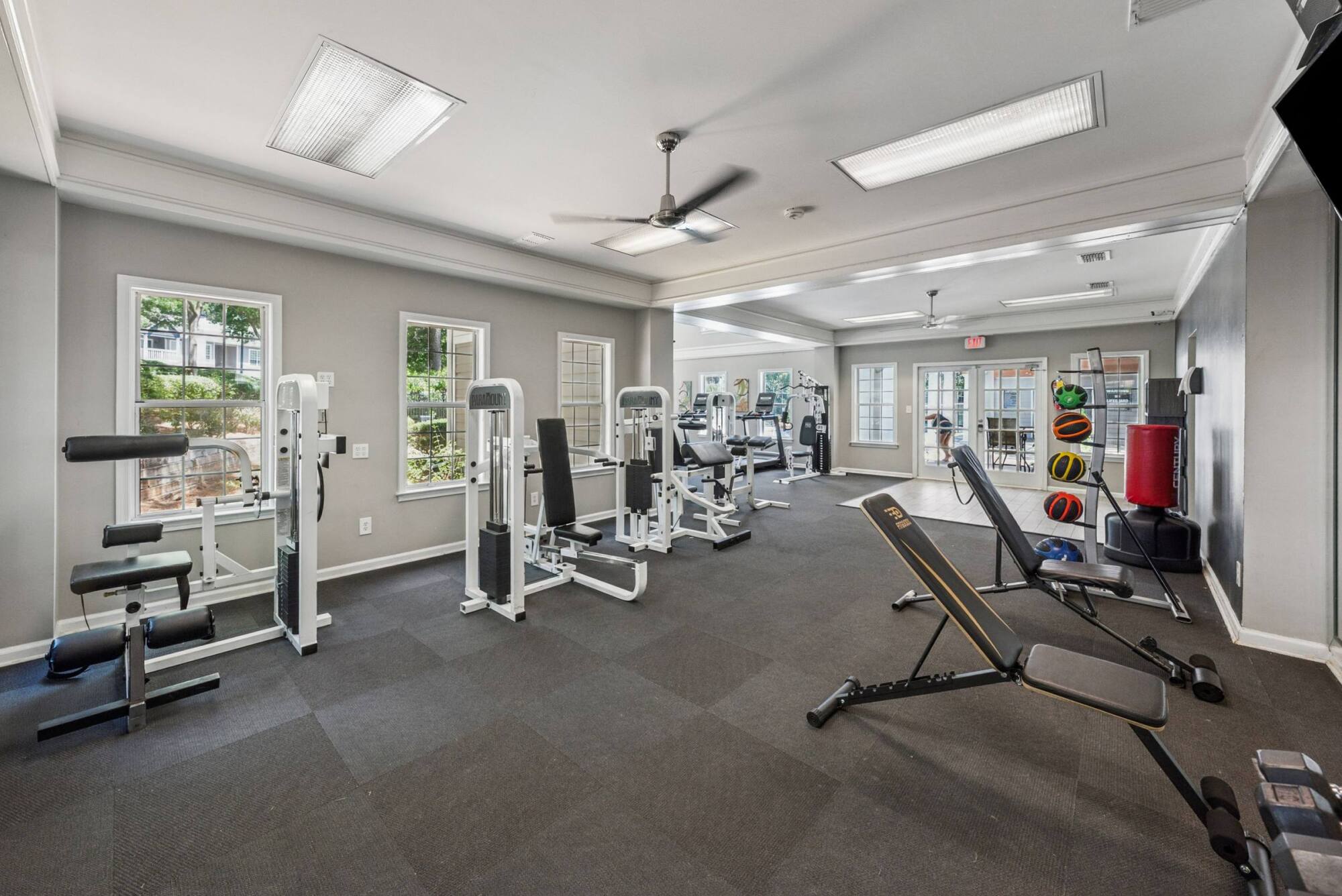 Bright gym with weight machines, benches, free weights, and large windows letting in natural light.