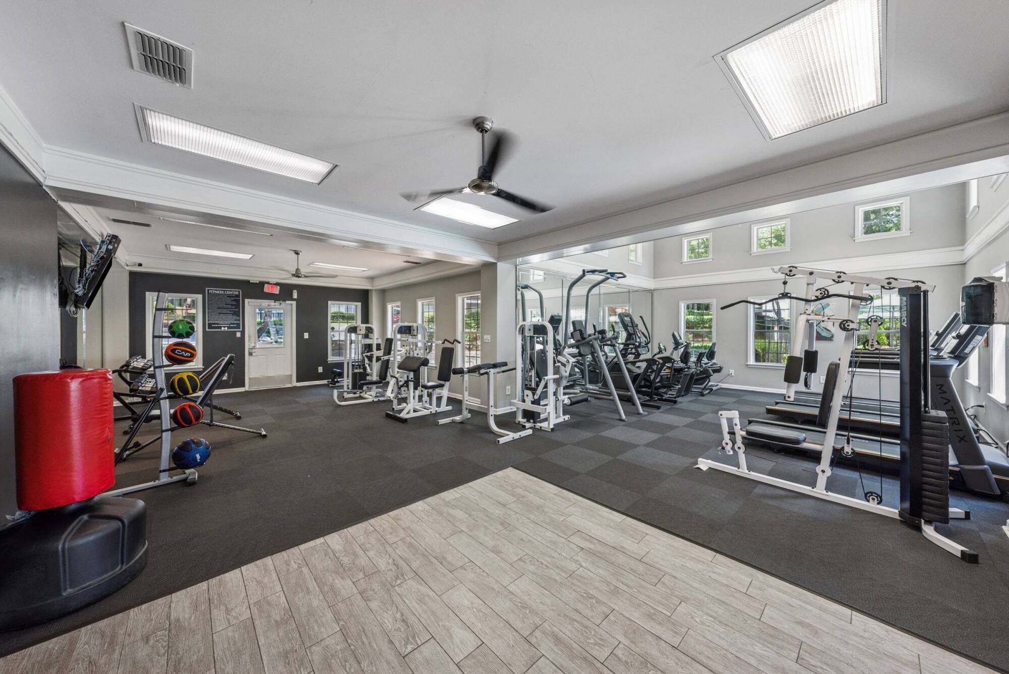 Bright gym with weight machines, cardio equipment, punching bag, and large windows letting in natural light.