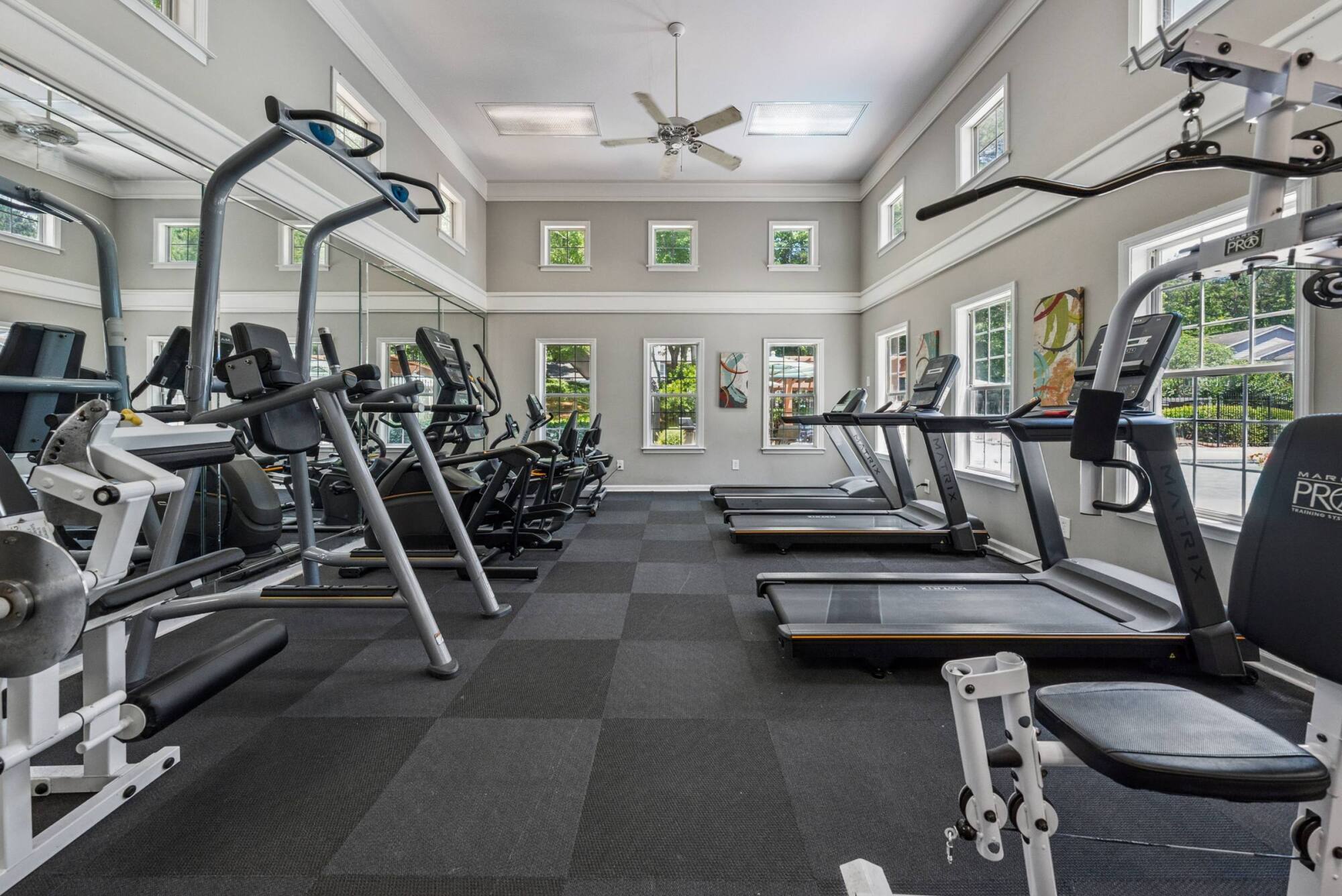 Modern gym with treadmills, exercise bikes, and strength equipment in a bright room with large windows.