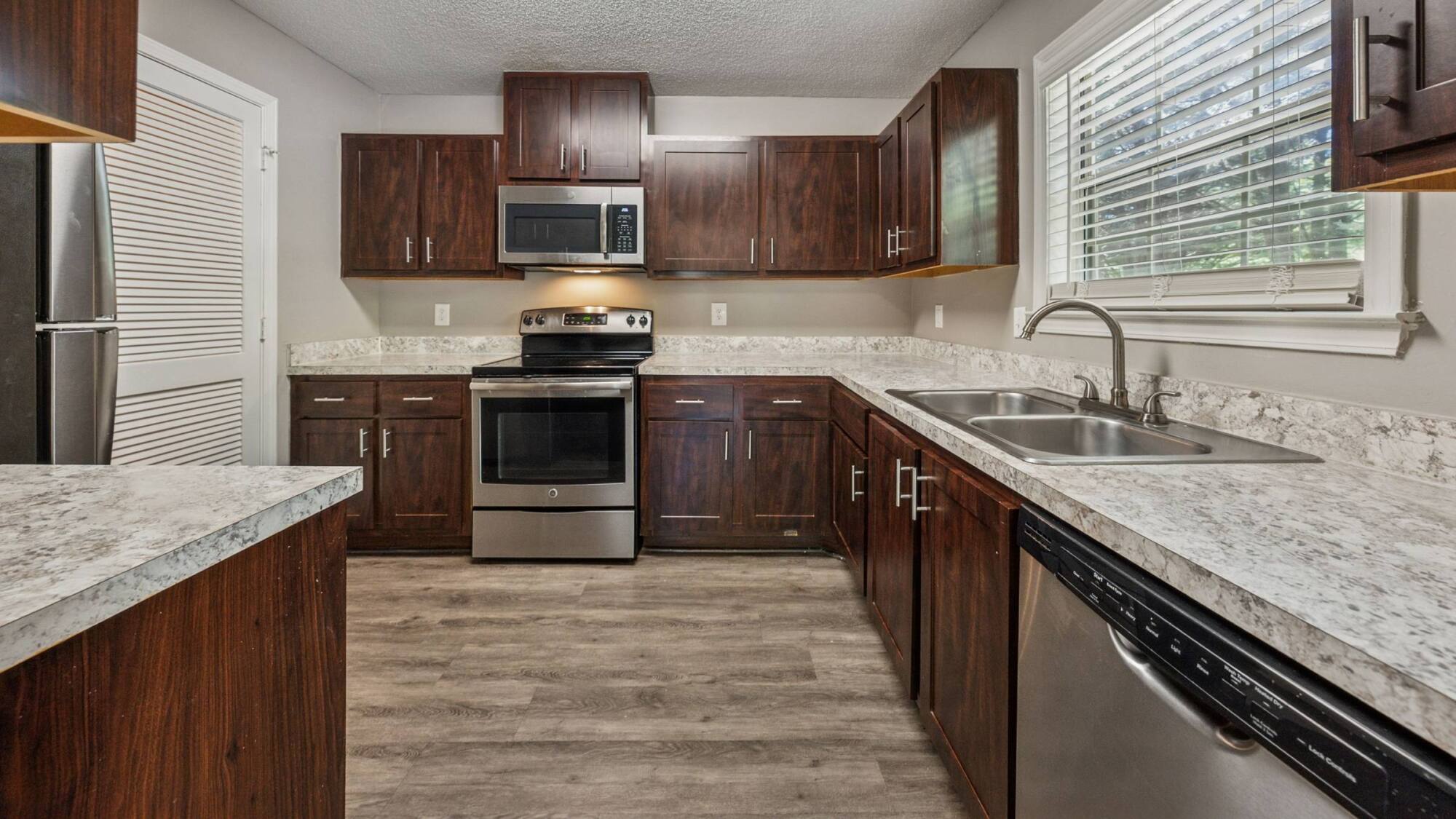 Modern kitchen with dark wood cabinets, stainless steel appliances, and marble-patterned countertops.