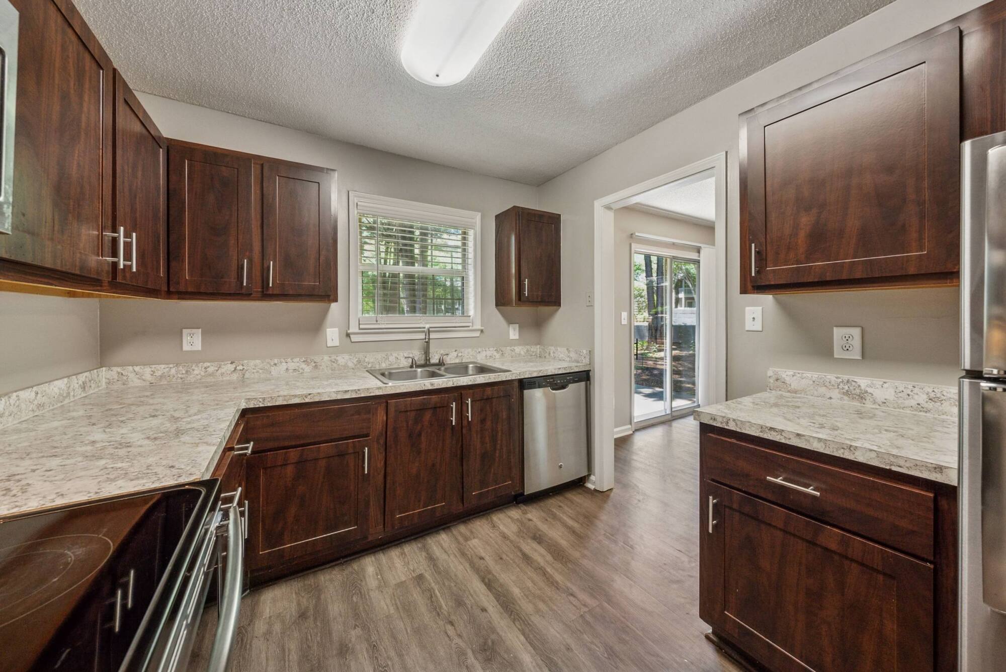 Modern kitchen with dark wood cabinets, marble countertops, stainless steel appliances, and a window over the sink.