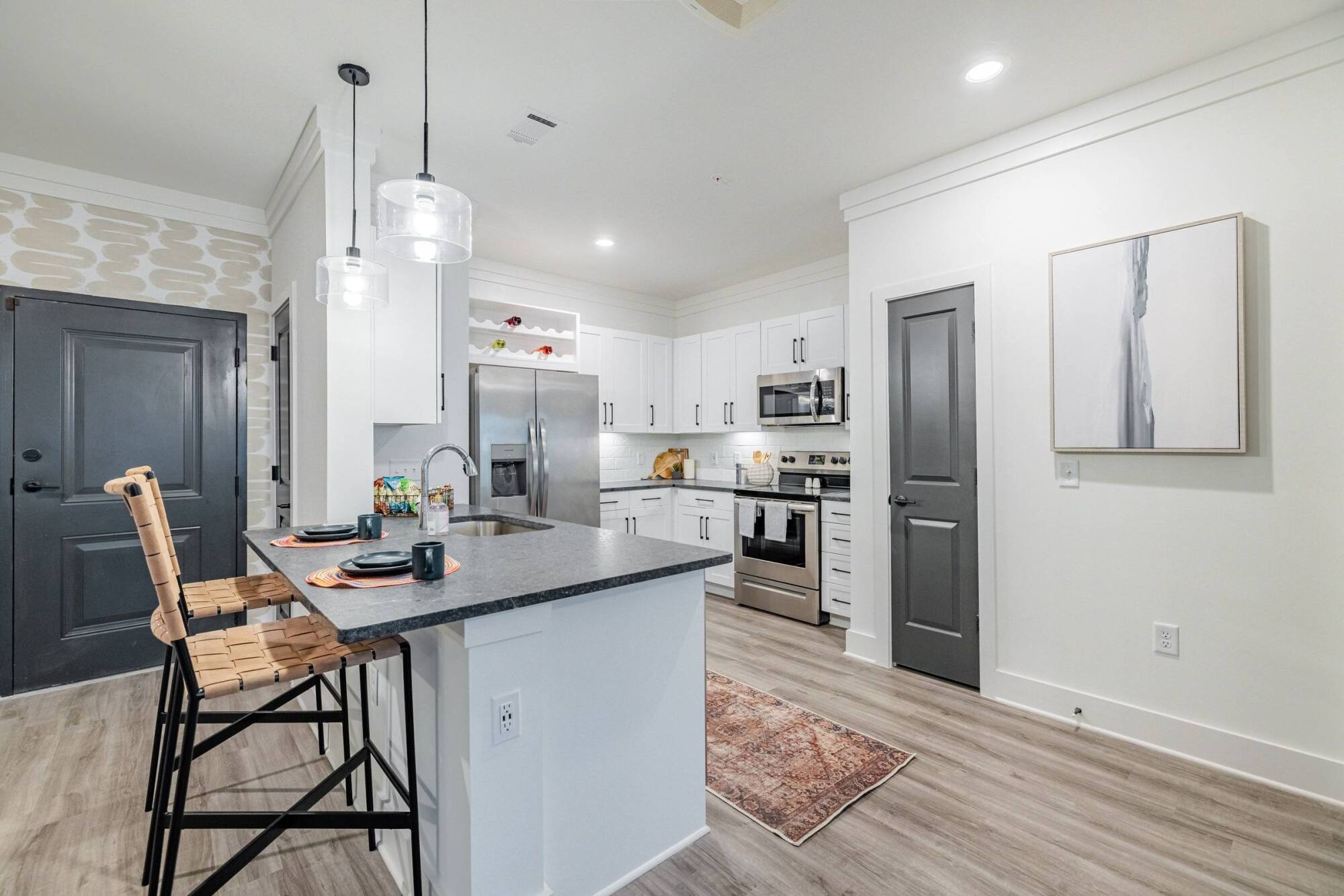 Modern kitchen with white cabinets, stainless steel appliances, and a breakfast bar with two woven stools.