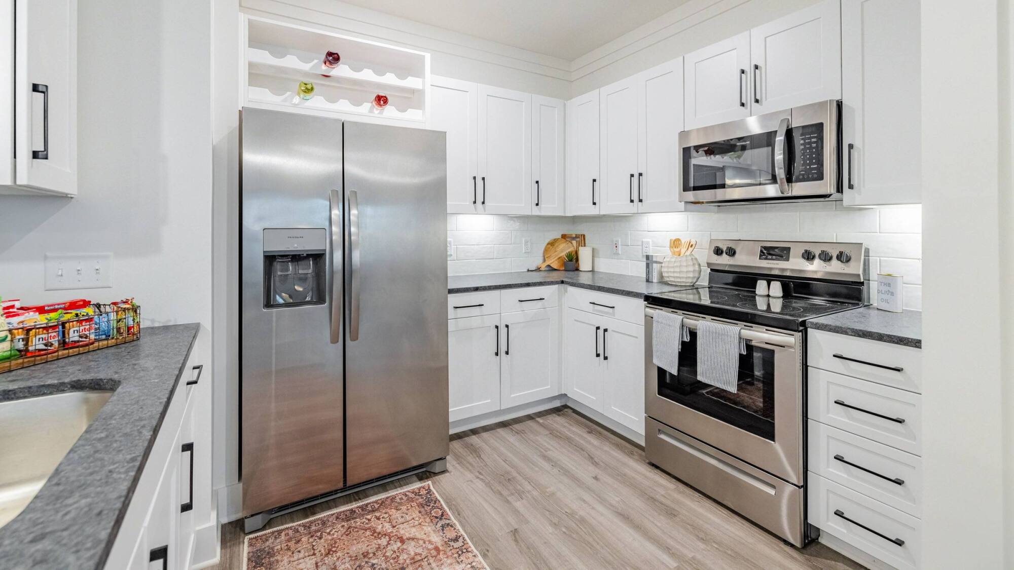Modern kitchen with white cabinets, stainless steel appliances, and a rug on wood flooring.