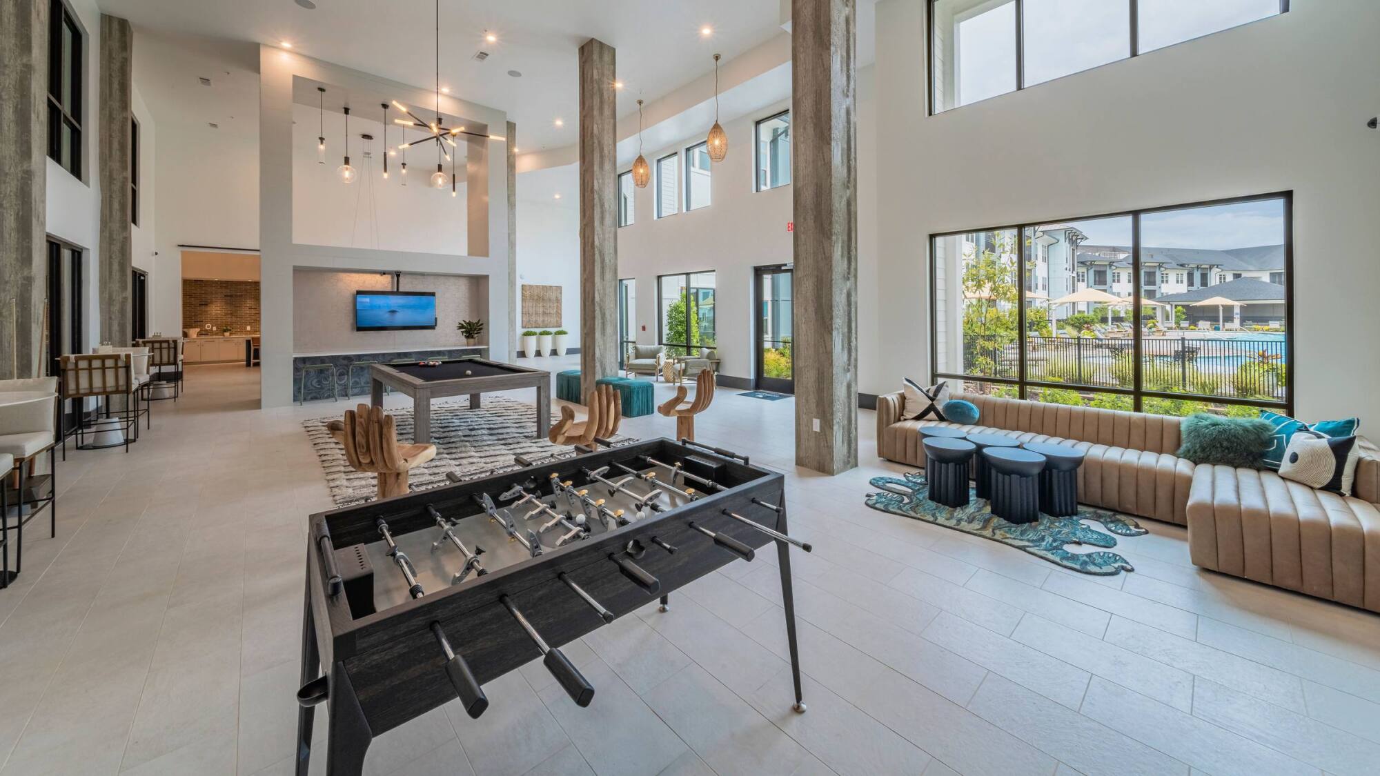 Modern, spacious lounge with foosball, pool table, sofas, large windows, and high ceilings.