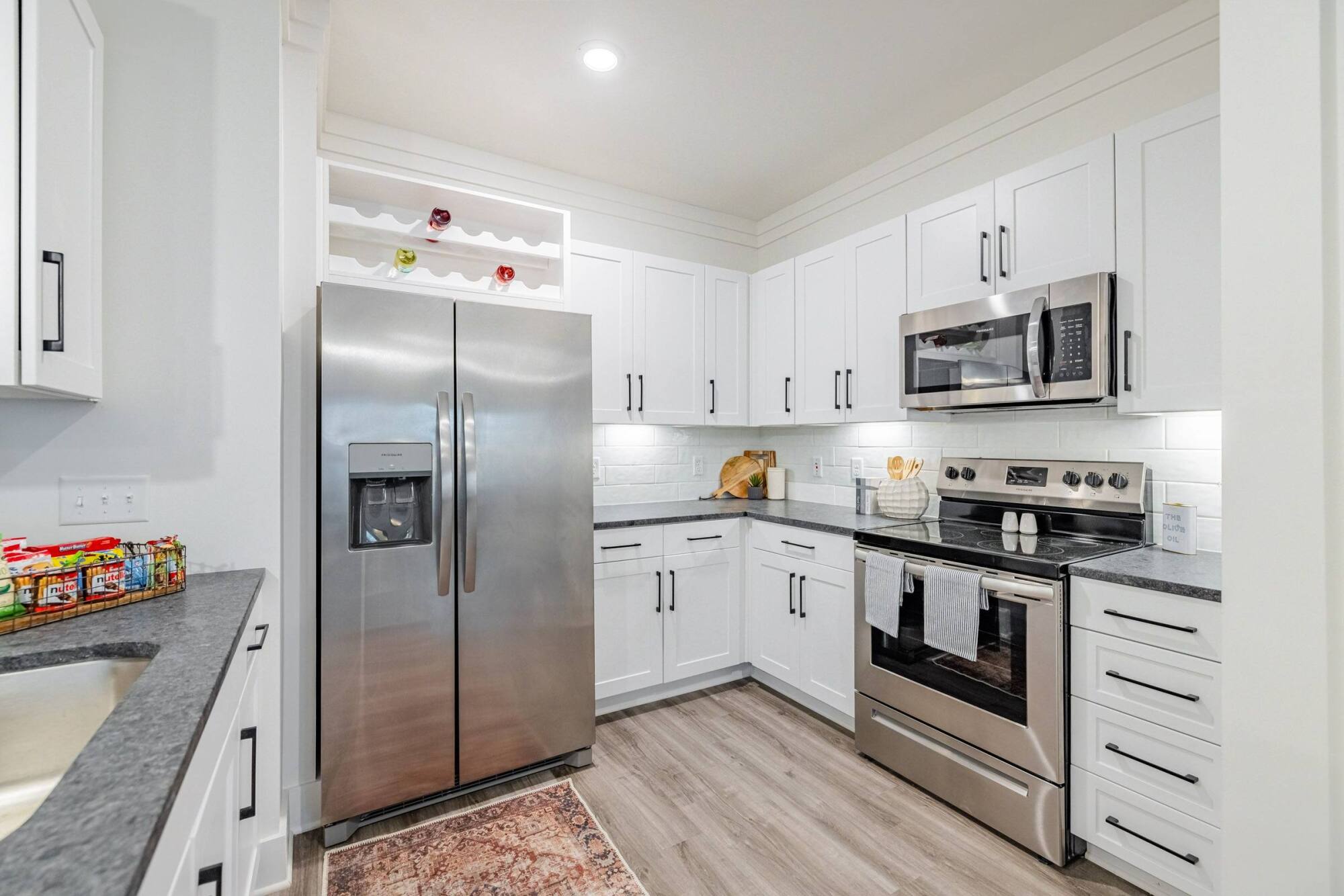 Modern kitchen with white cabinets, stainless steel appliances, and light wood flooring.