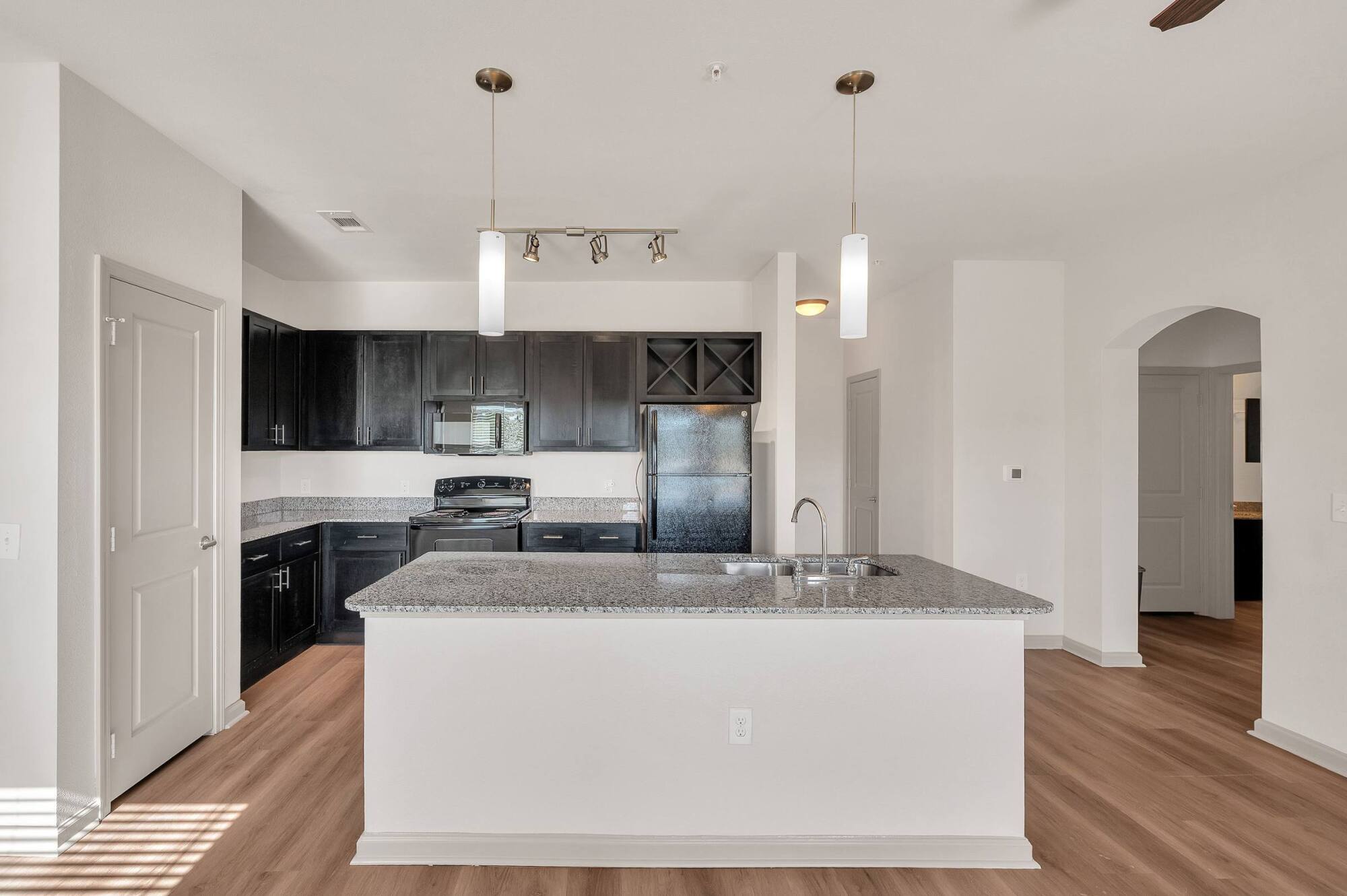 Modern kitchen with dark cabinets, granite island, black appliances, and wood flooring.