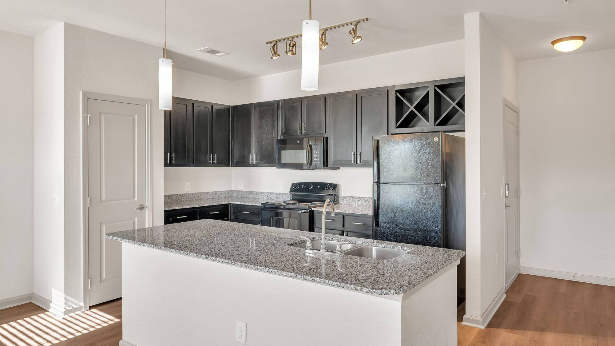 Modern kitchen with dark cabinets, granite countertops, island with sink, and black appliances.