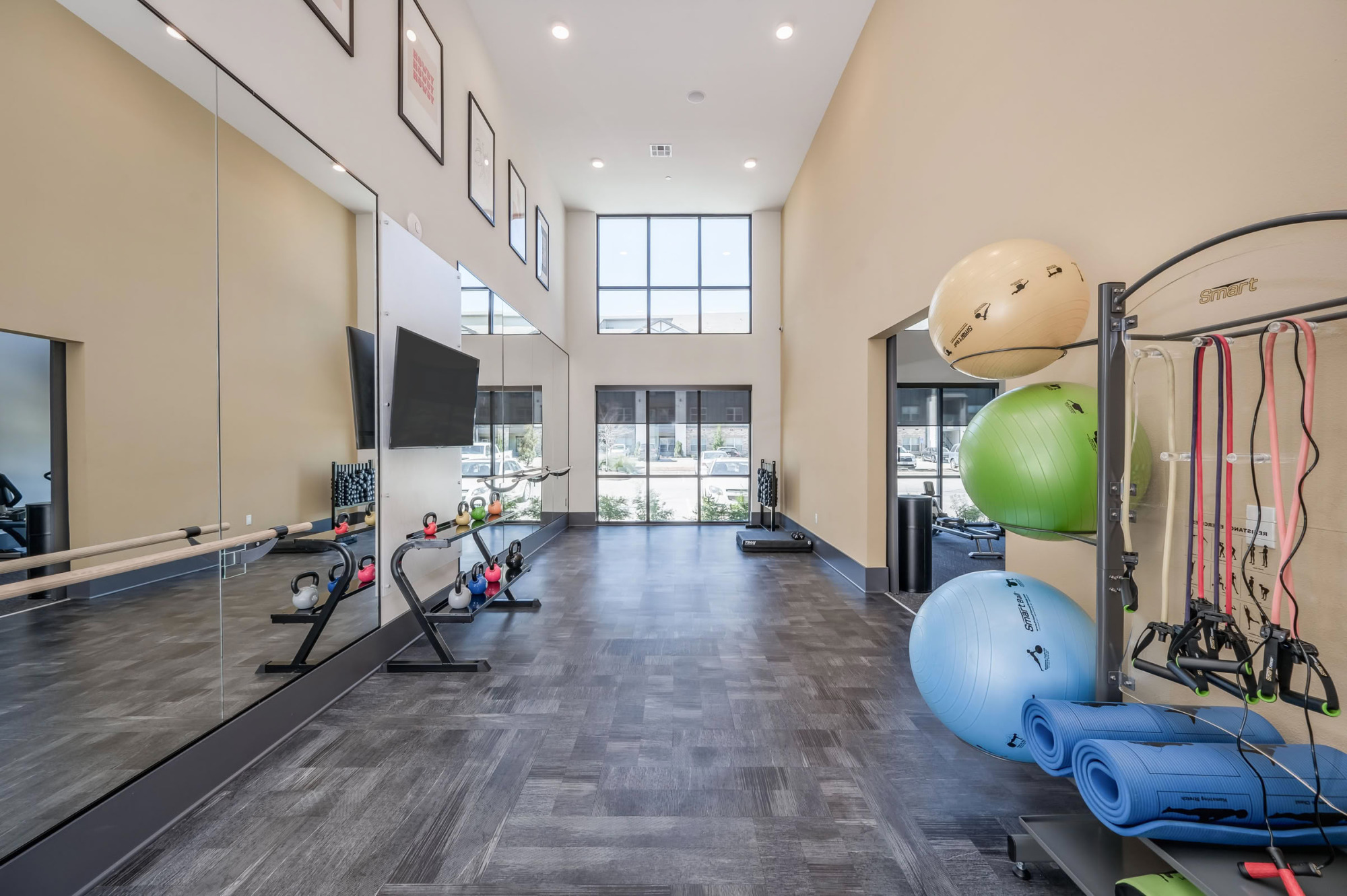 Yoga and stretching studio with mirrored walls, a barre, dark wood-look flooring, stationary bikes, stability balls, resistance bands, and rolled exercise mats.