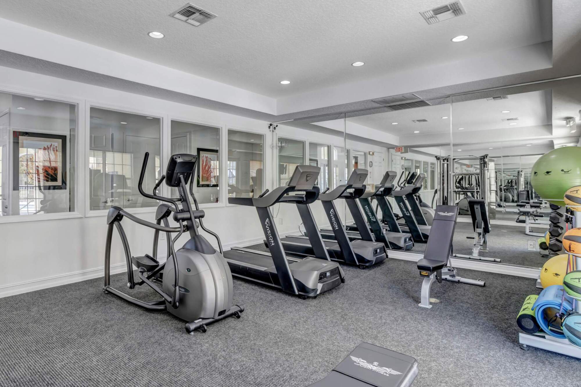 Modern gym with treadmills, elliptical machine, exercise balls, and large mirrors on the wall.
