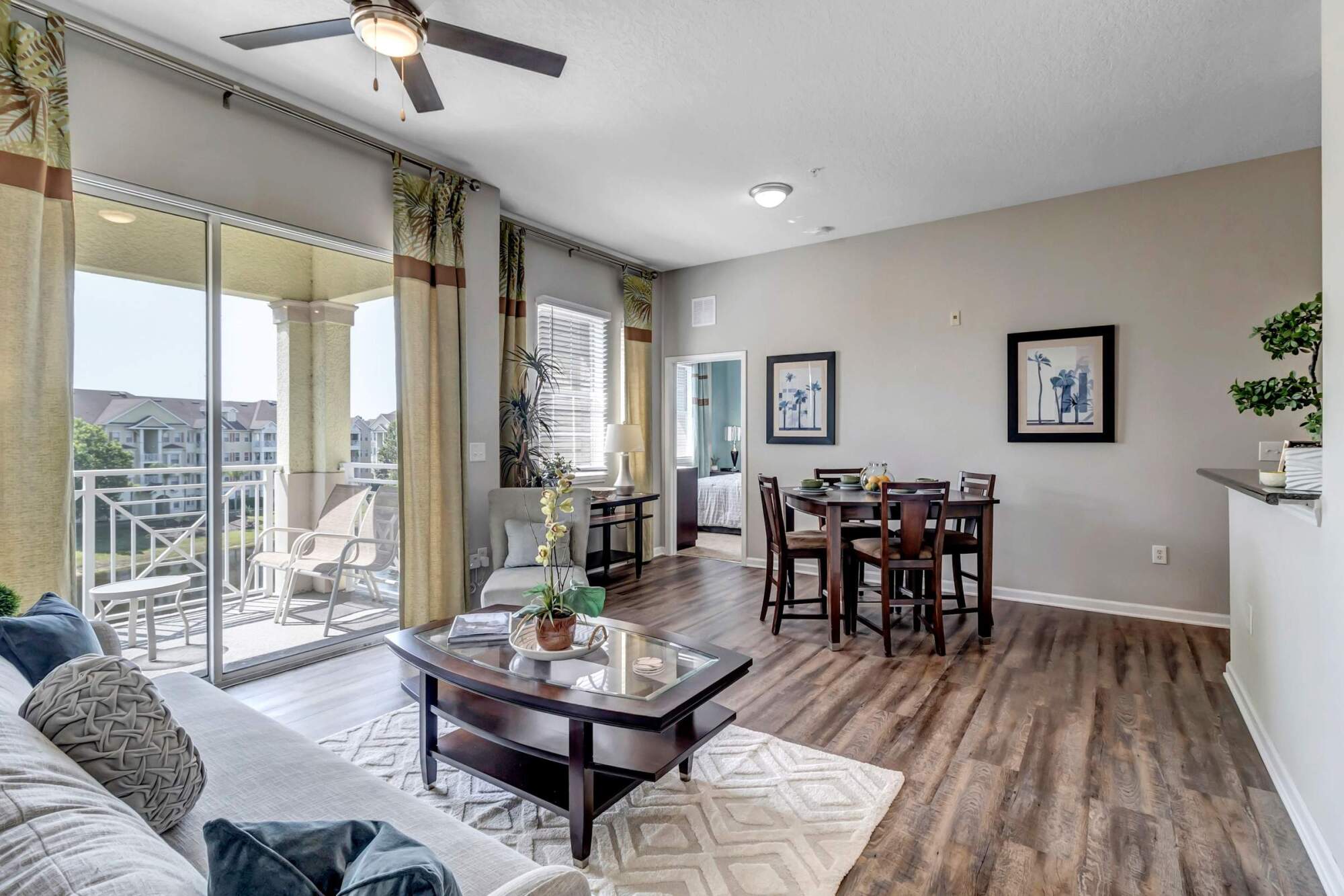 Modern living and dining area with wood floors, neutral decor, and glass doors opening to a balcony.