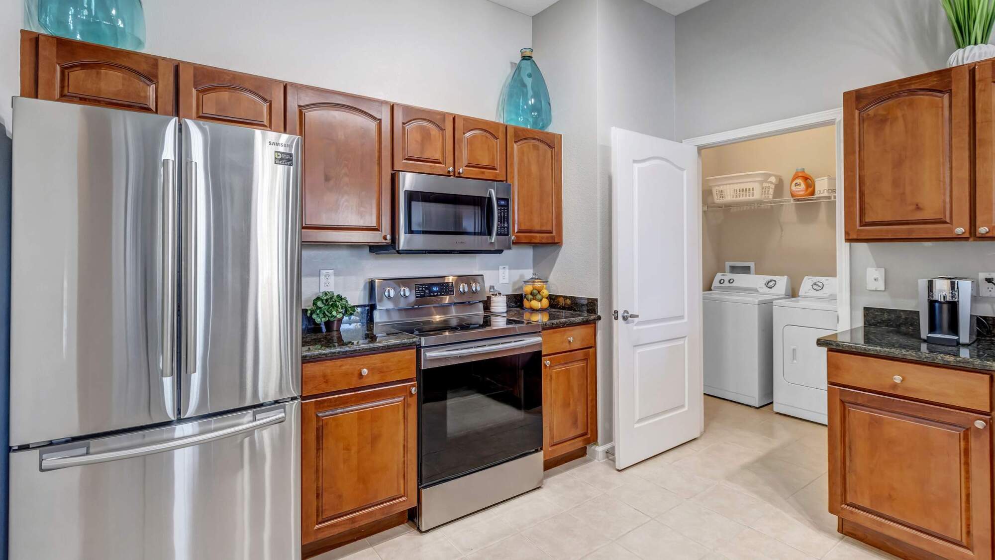 Modern kitchen with stainless steel appliances, wooden cabinets, and an open door to a laundry room with washer and dryer.
