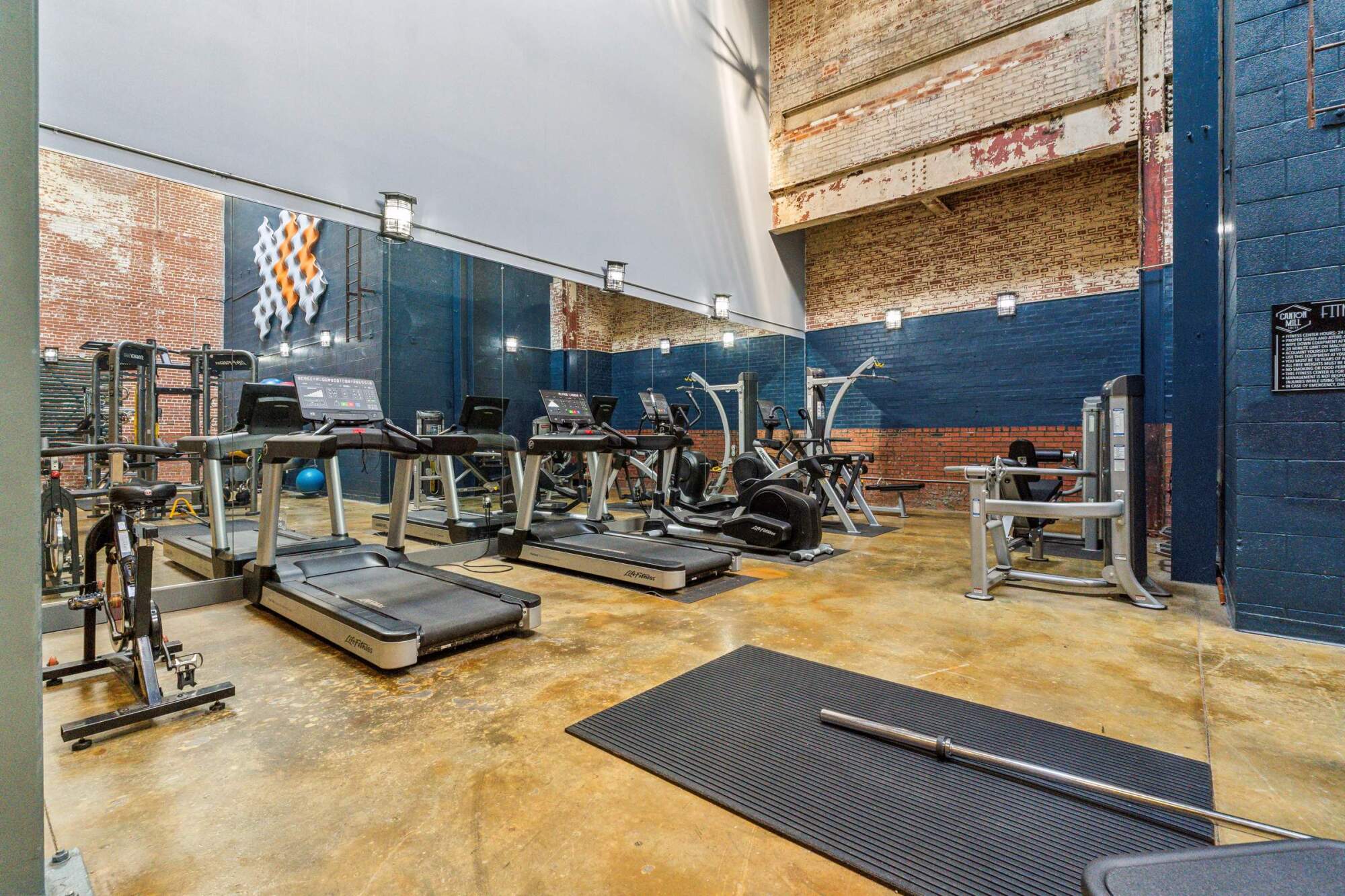 Modern gym with treadmills, weight machines, a black mat, and exposed brick walls.