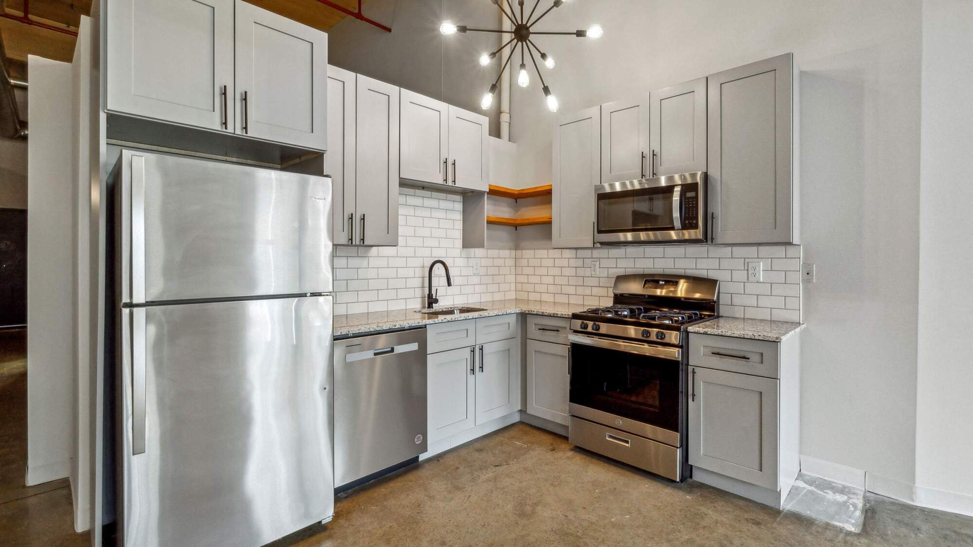 Modern kitchen with stainless steel appliances, gray cabinets, white subway tile, and a stylish light fixture.