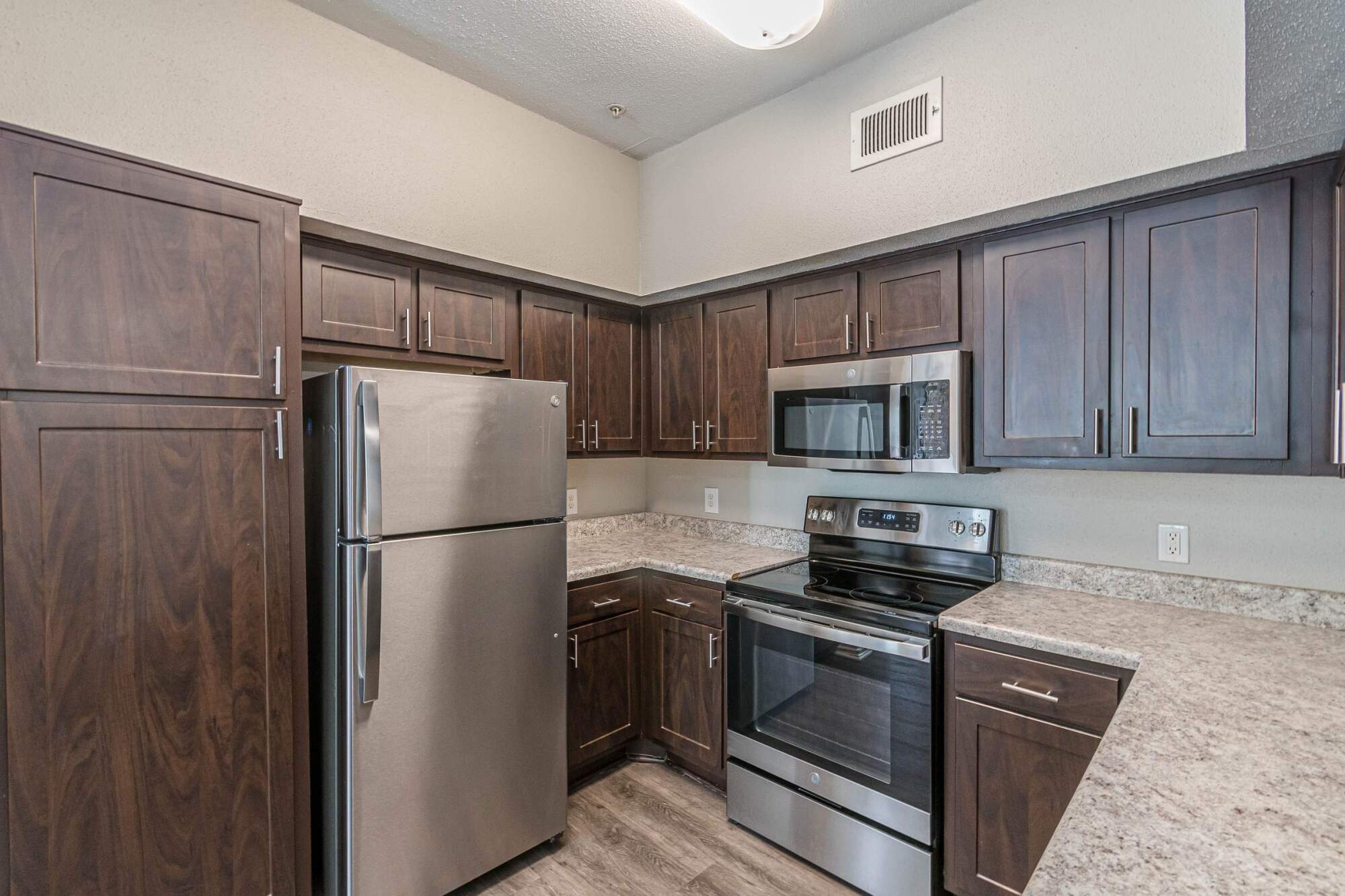 Modern kitchen with dark wood cabinets, stainless steel appliances, and light granite countertops.