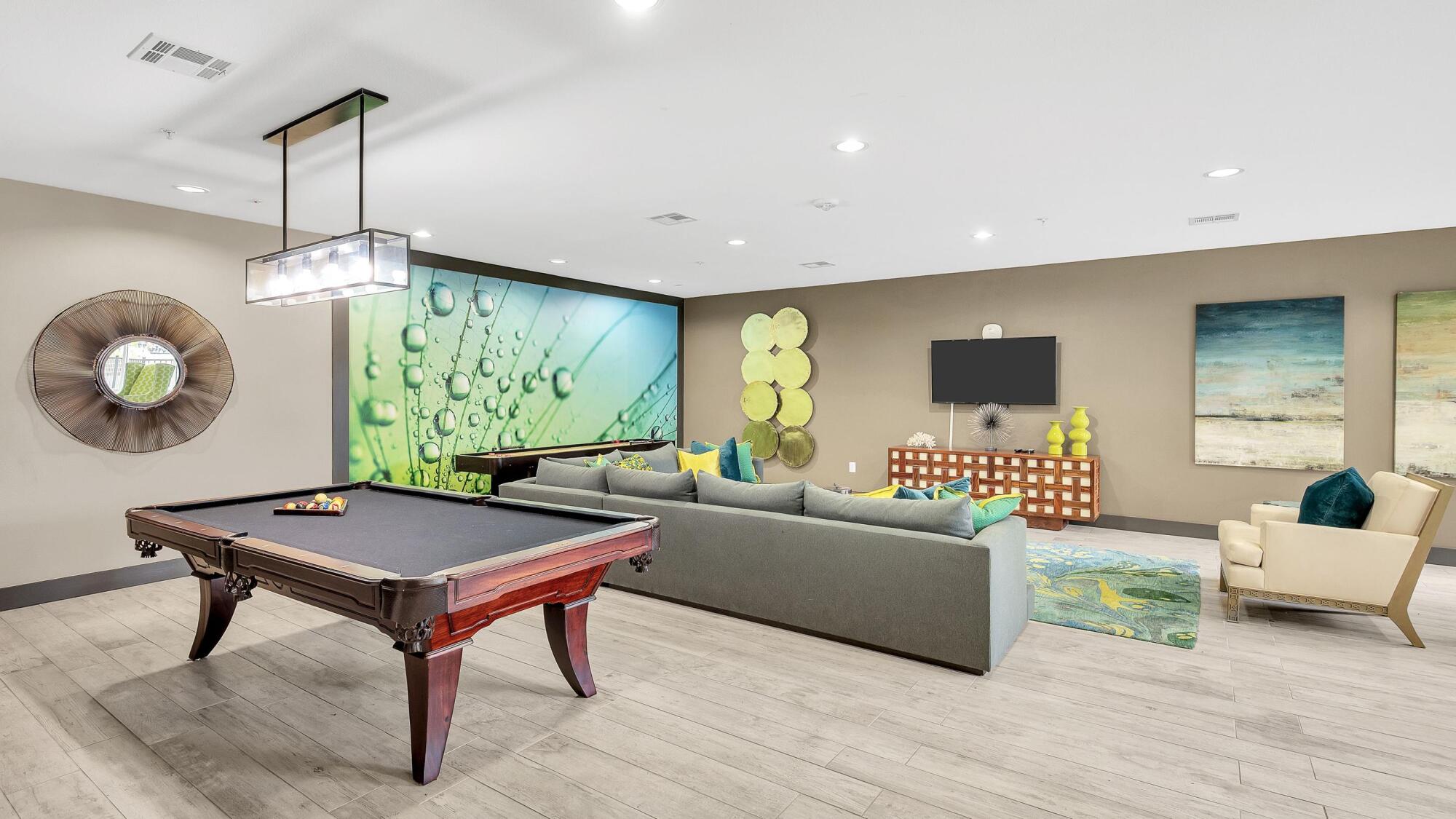 Modern game room with a pool table, sectional sofa, wall art, TV, and green decorative accents.