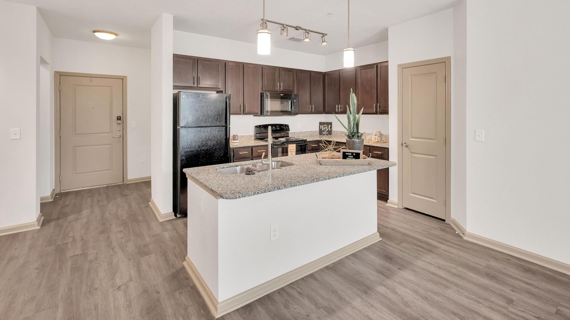 Modern kitchen with dark cabinets, granite island, black appliances, and wood-style flooring.