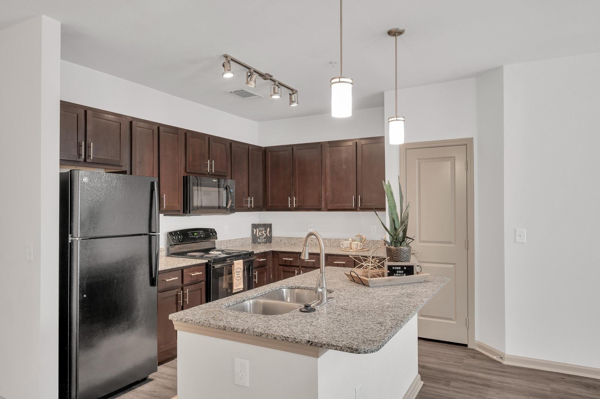 Modern kitchen with dark cabinets, granite countertops, black appliances, and pendant lighting over an island.