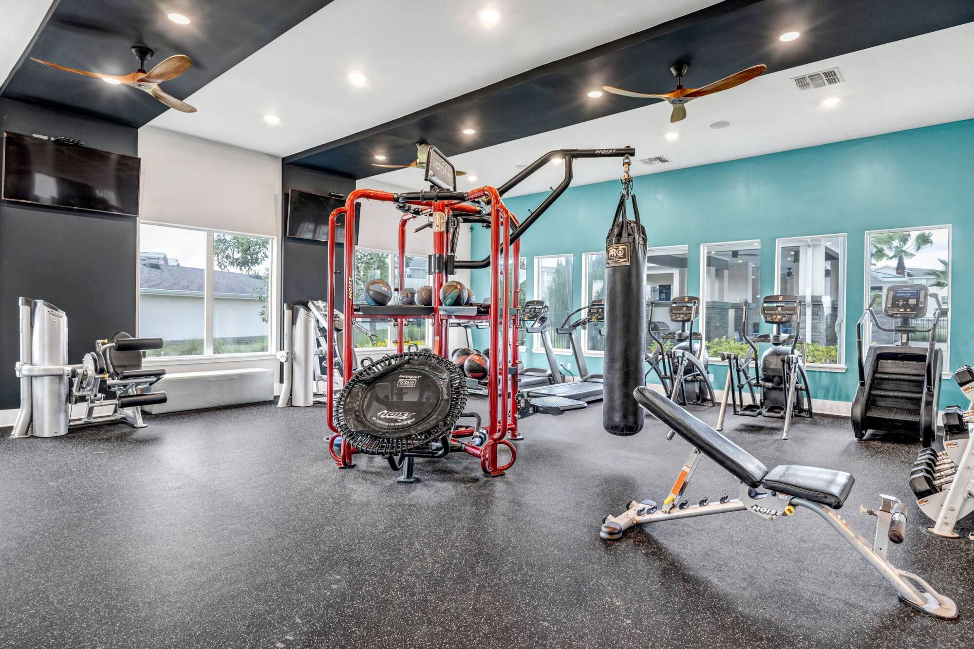 Modern gym with various exercise equipment, including cardio machines, weights, and a punching bag.