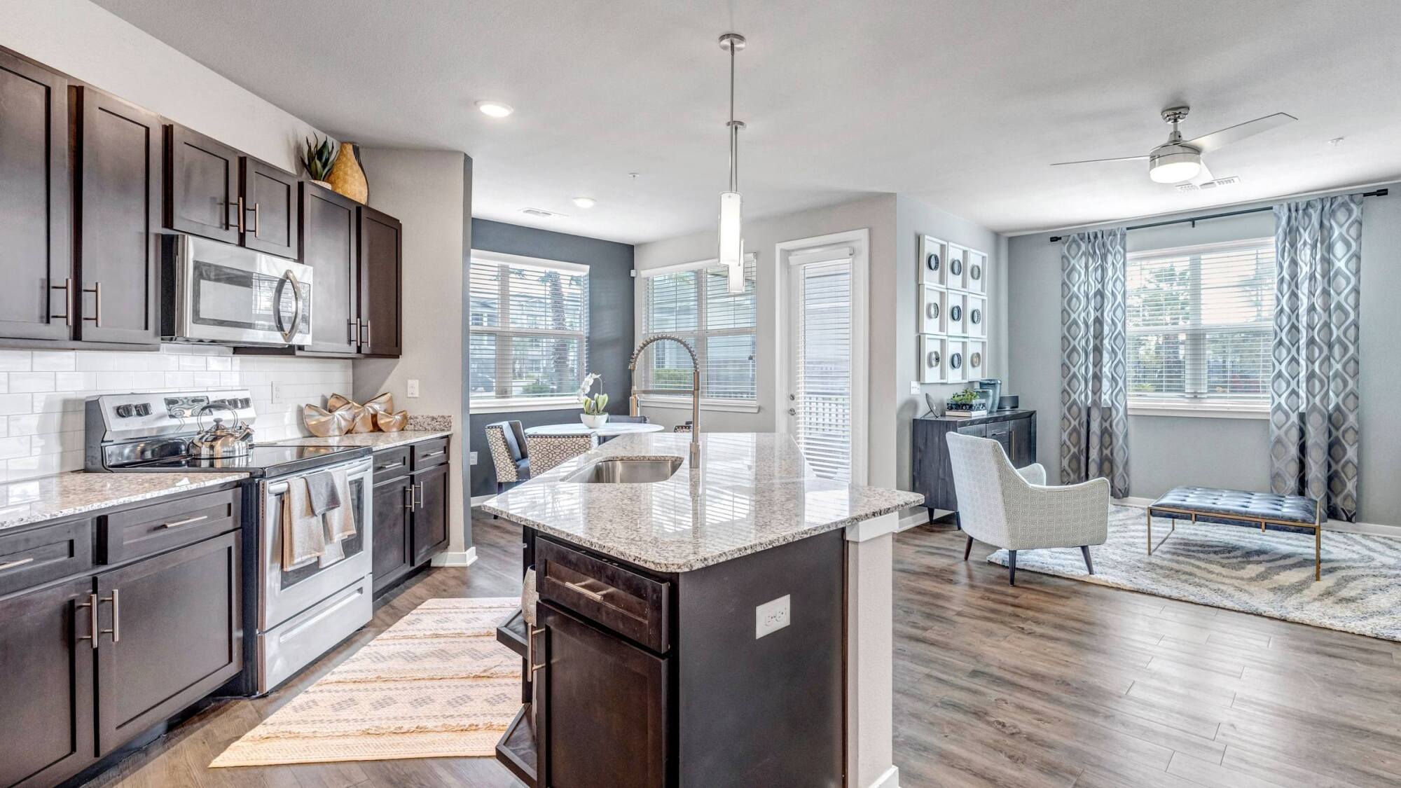 Modern open-concept kitchen and living area with dark cabinets, granite island, and large windows.