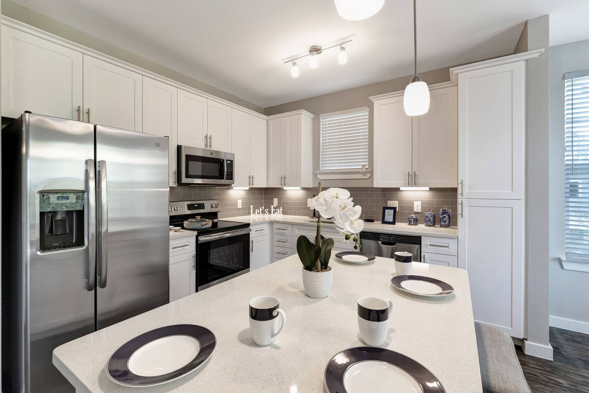 Modern kitchen with white cabinets, stainless appliances, and an island set with dishes and a potted orchid.