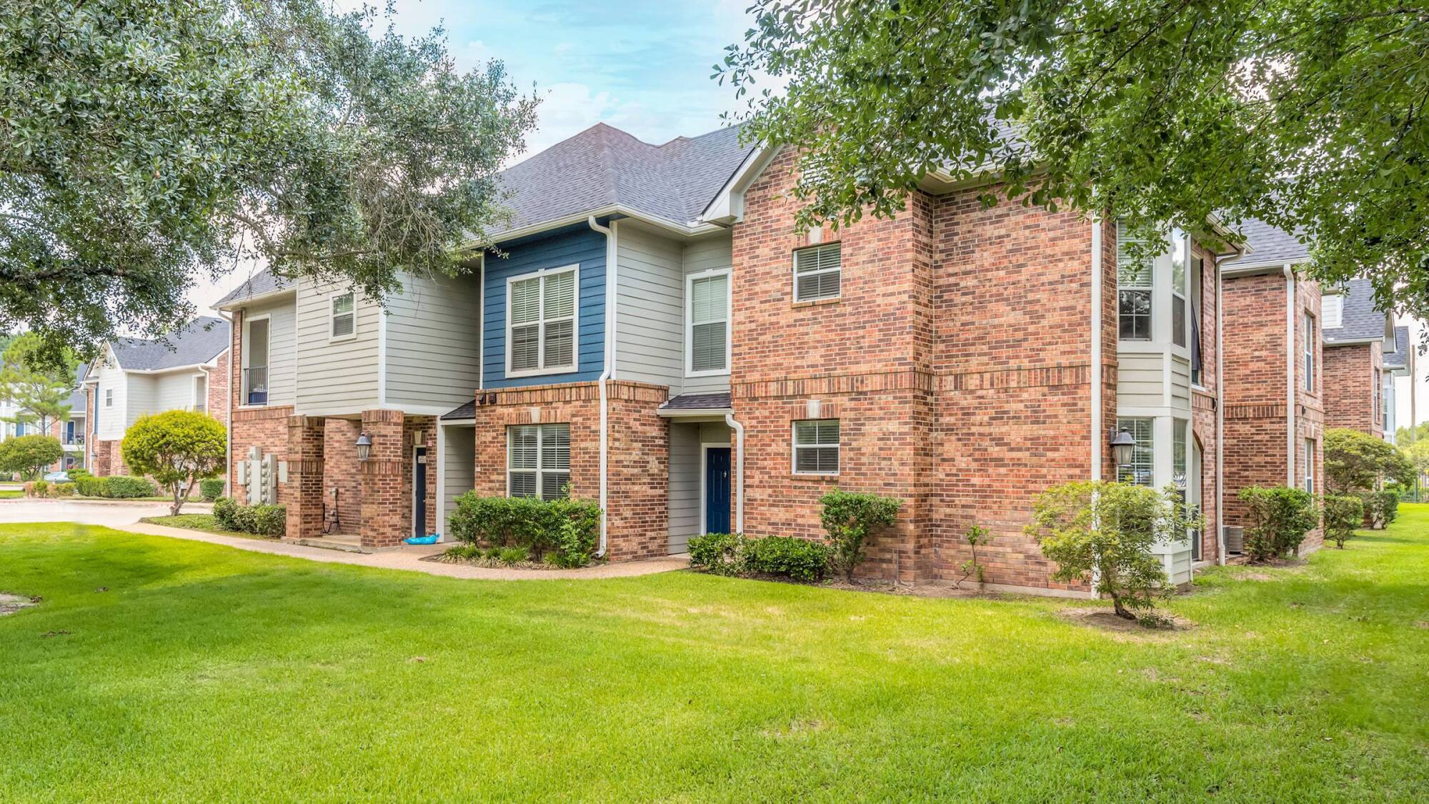 Two-story apartment building with brick and siding exterior, surrounded by green grass and trees.