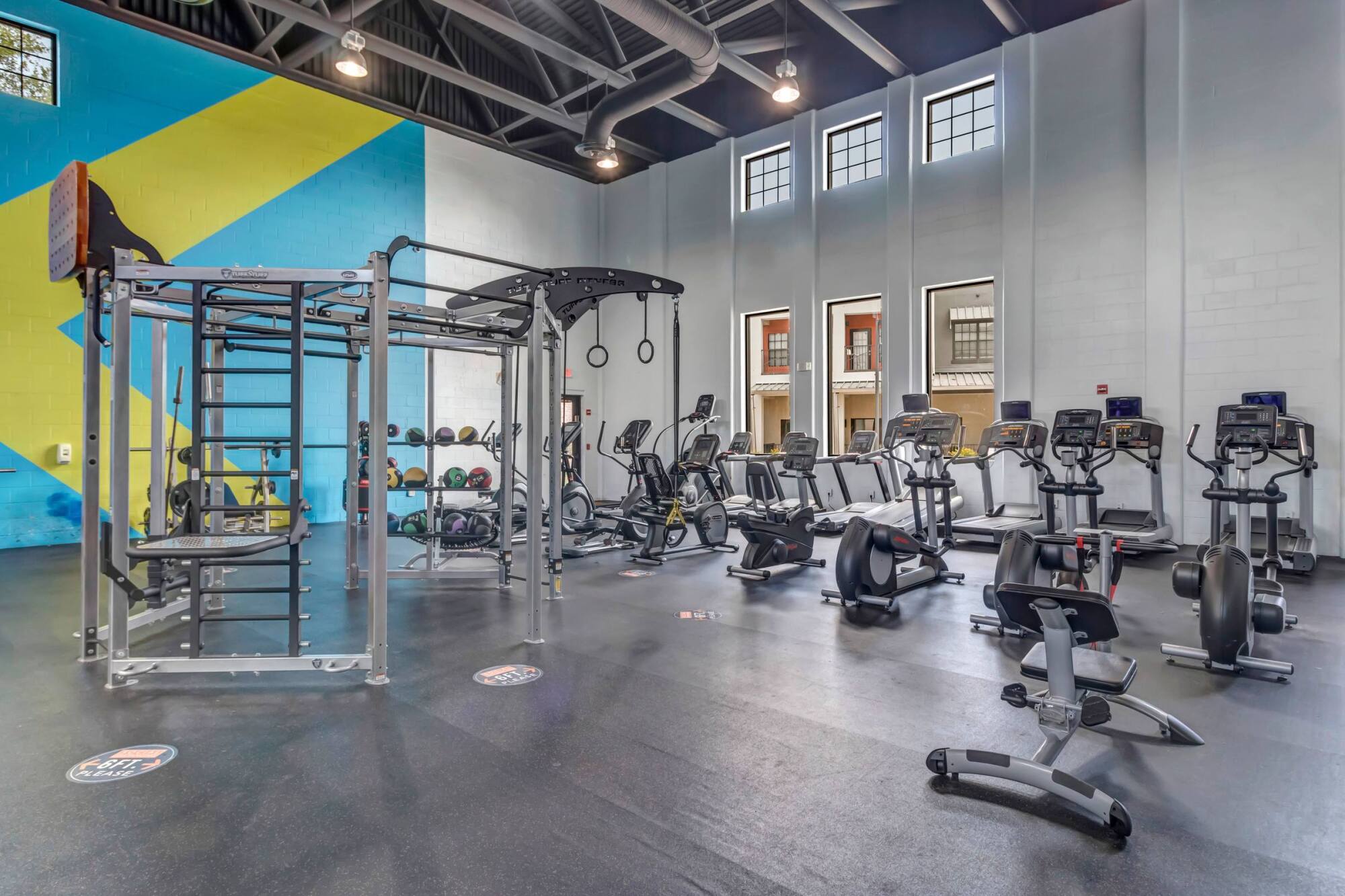 Spacious gym with cardio machines, weight equipment, and high ceilings with large windows.