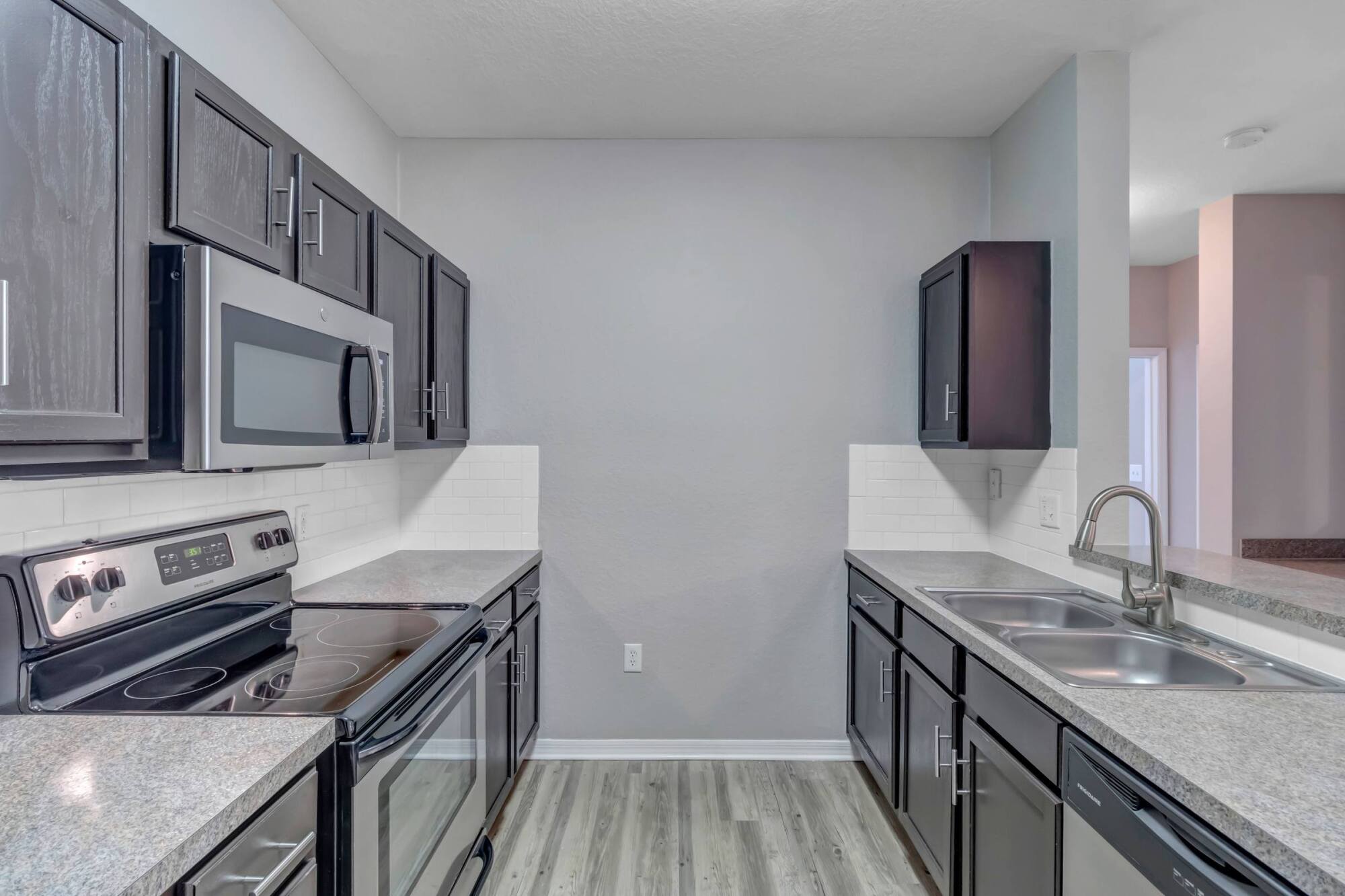 Modern kitchen with gray cabinets, stainless steel appliances, and light wood flooring.