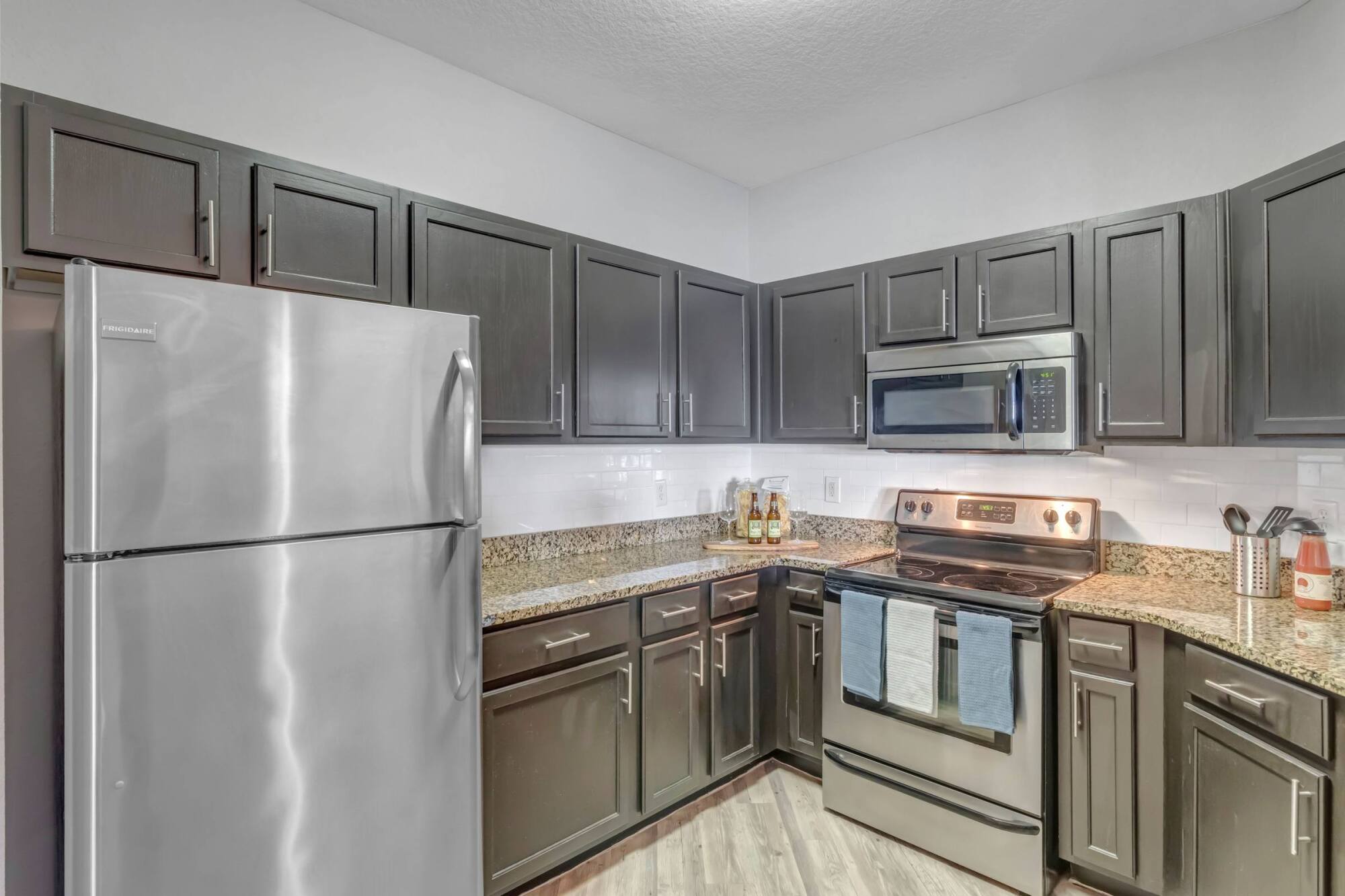 Modern kitchen with dark cabinets, stainless steel appliances, granite countertops, and wood-look flooring.