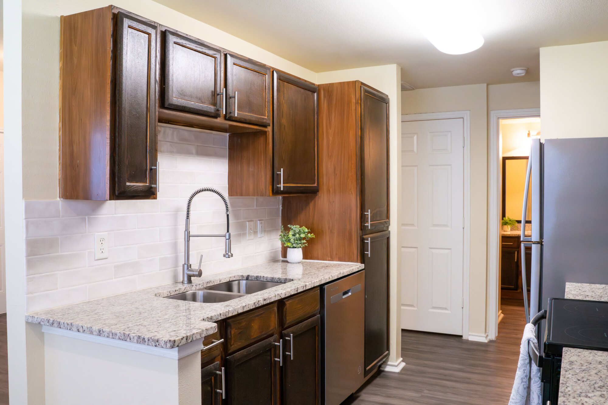 Kitchen detail with knotty wood cabinets, white subway tile backsplash, granite countertops, a tall industrial-style faucet over a stainless steel sink, and gray wood-look flooring.