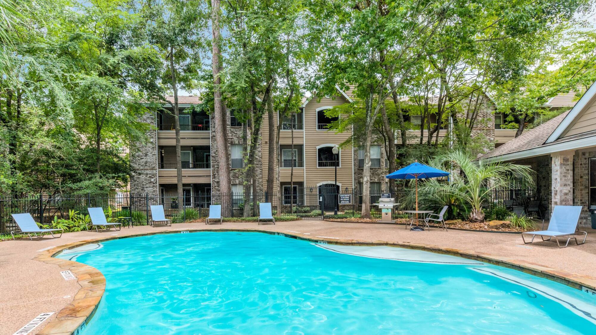 Swimming pool at Forest View in The Woodlands, TX with lounge chairs, a grilling station, and apartment balconies beyond the pines.