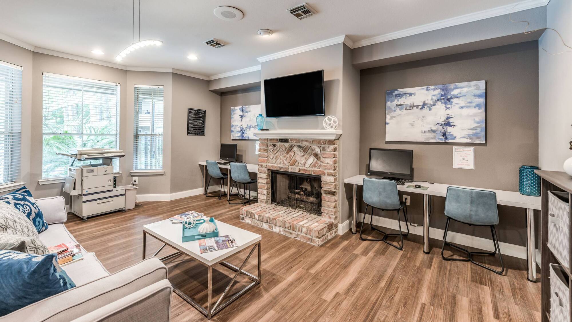Resident lounge and business center at Forest View with a brick fireplace, mounted TV, and two computer workstations.