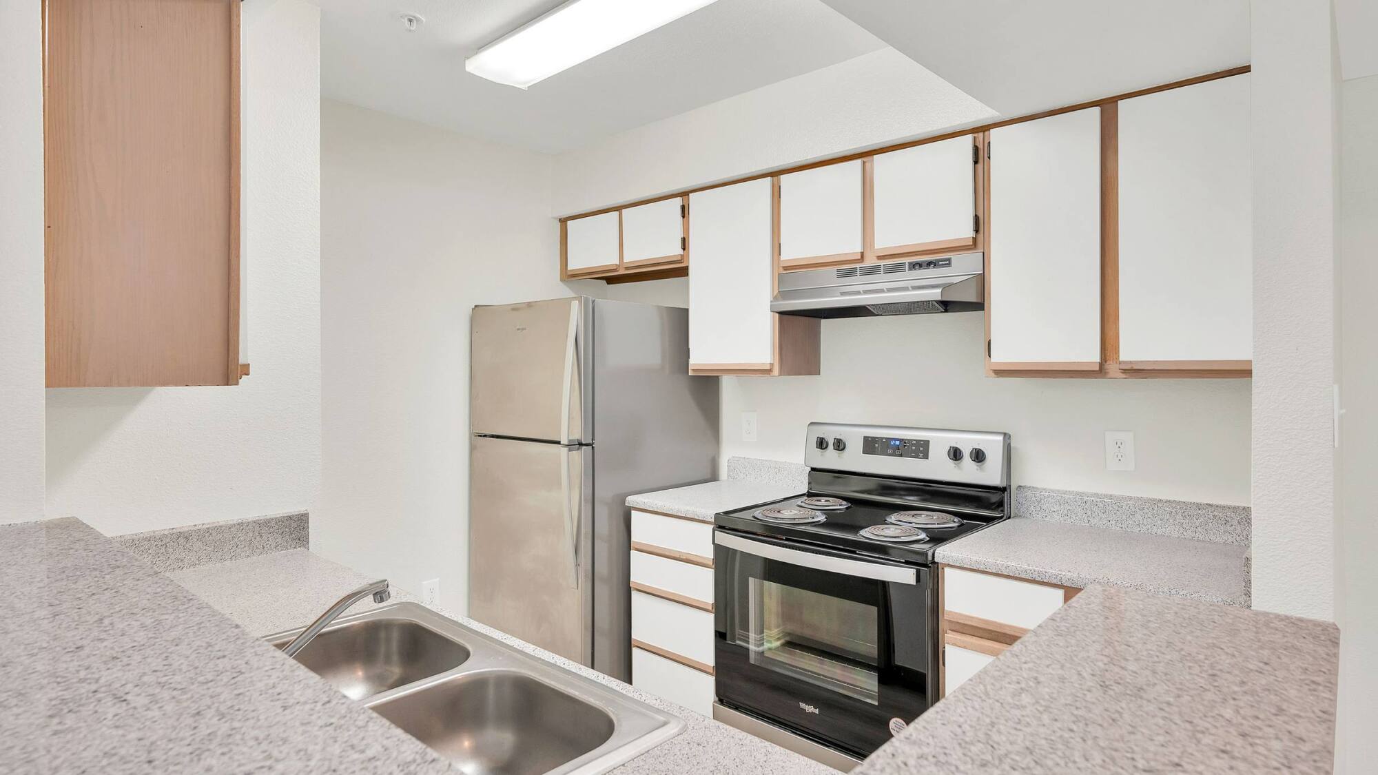 Kitchen at Forest View in The Woodlands, TX with a stainless steel range and refrigerator, white cabinets, and a double sink.