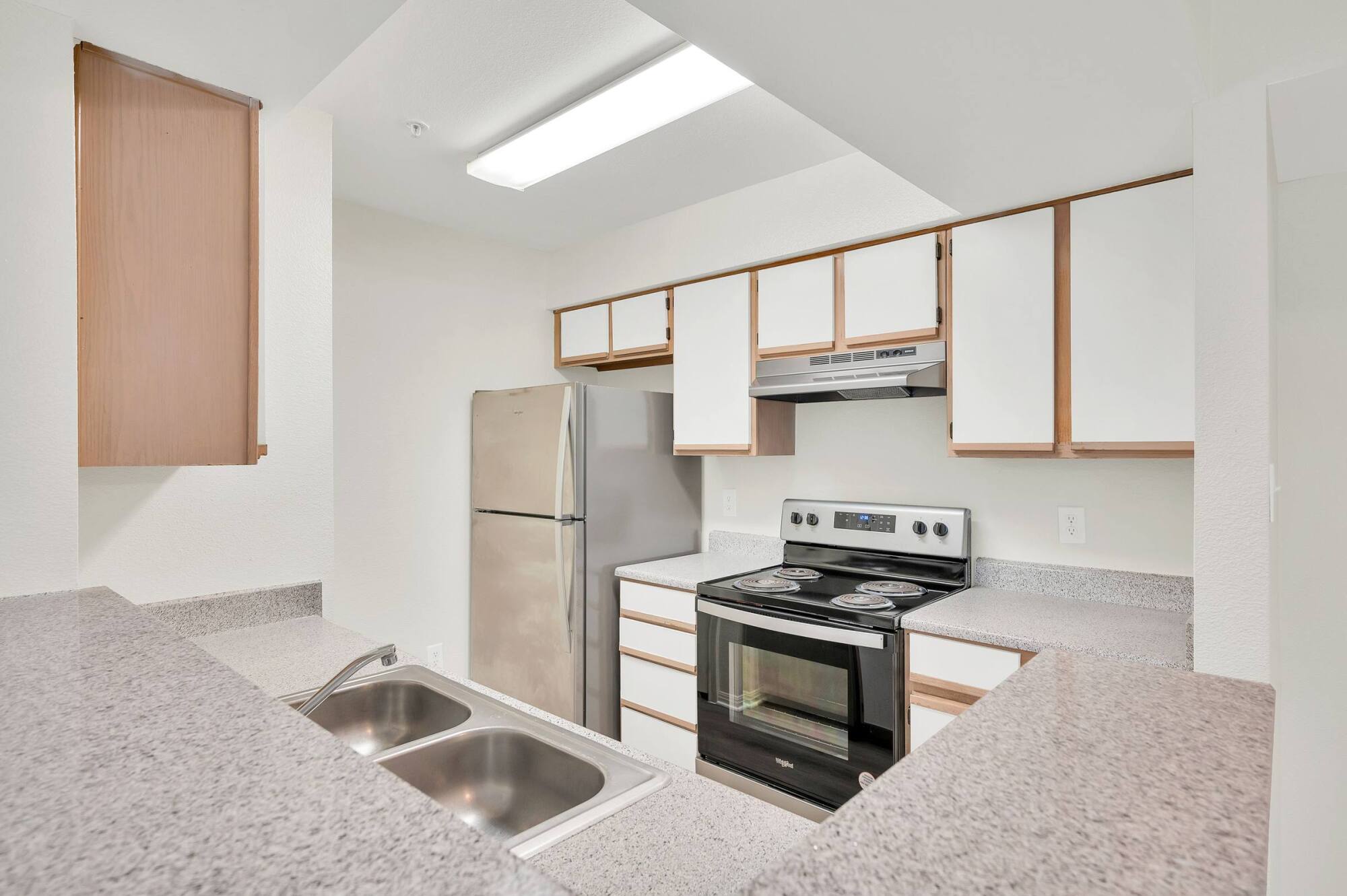 Forest View apartment kitchen featuring a stainless steel range and refrigerator, ample cabinets, and bright overhead lighting.
