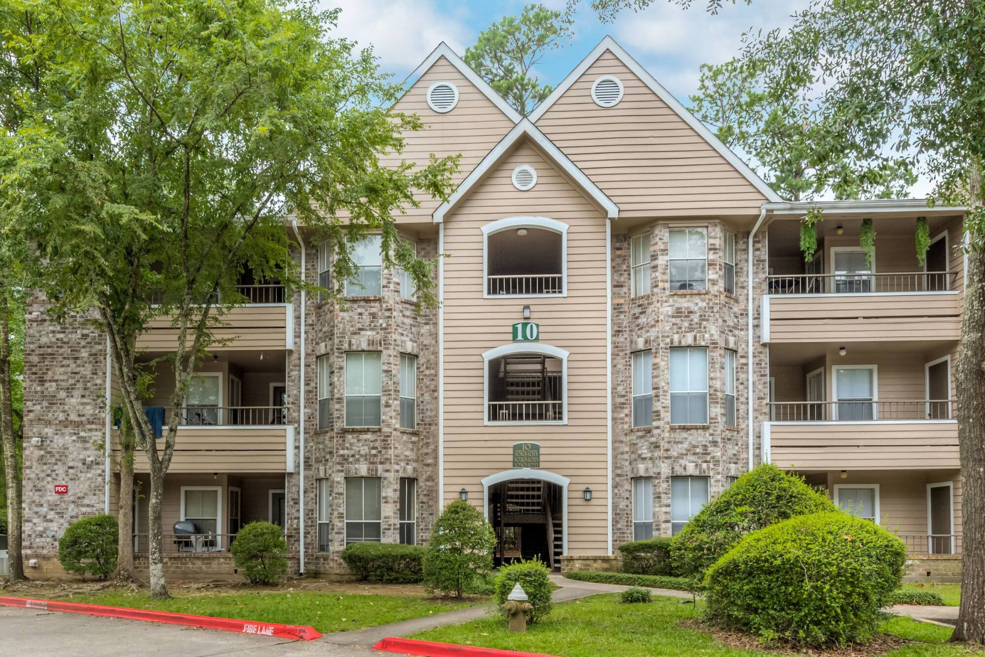 Brick and siding exterior of a Forest View apartment building in The Woodlands, TX, framed by mature trees and manicured shrubs.