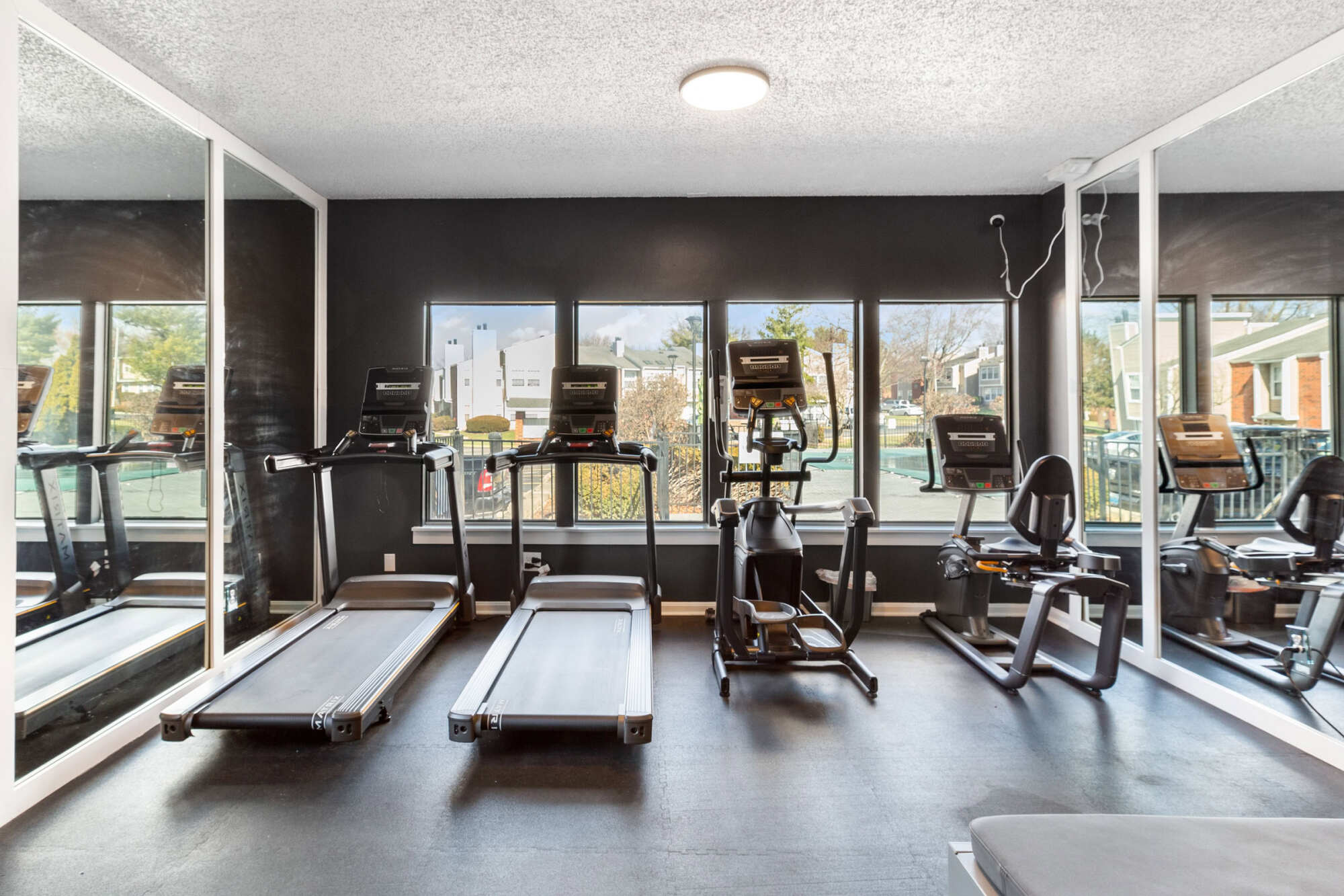 On-site fitness center with treadmills, an elliptical, and exercise equipment arranged in front of large windows with a mirrored wall and dark accent walls.