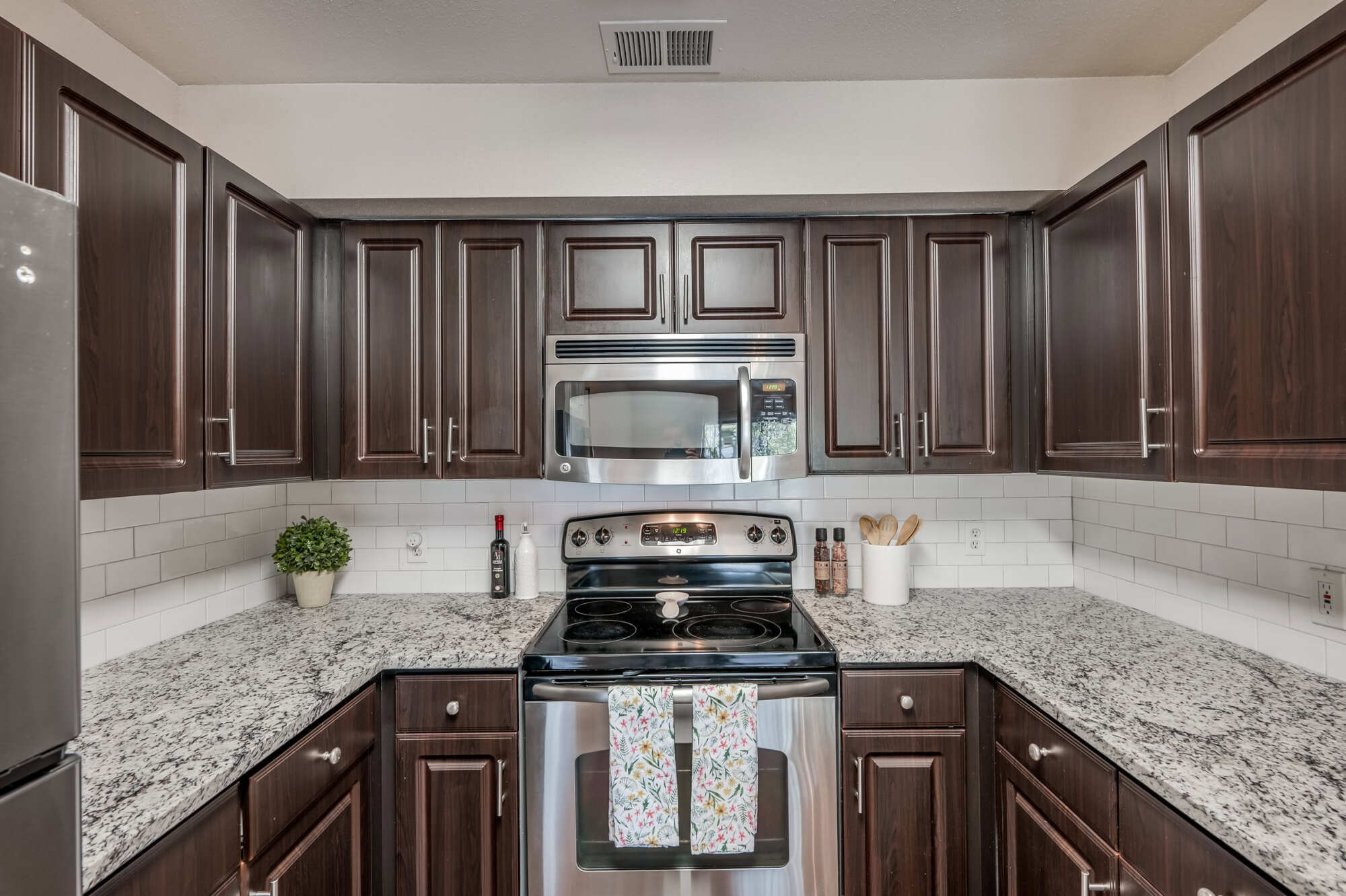 Apartment kitchen featuring dark wood cabinets, granite countertops, white subway tile backsplash, and stainless steel microwave, range, and refrigerator.