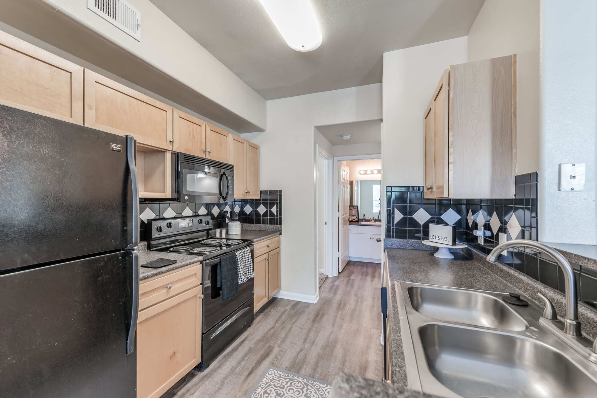 Apartment kitchen with maple cabinetry, granite countertops, black appliances, and a breakfast bar adjacent to a sunlit dining area.