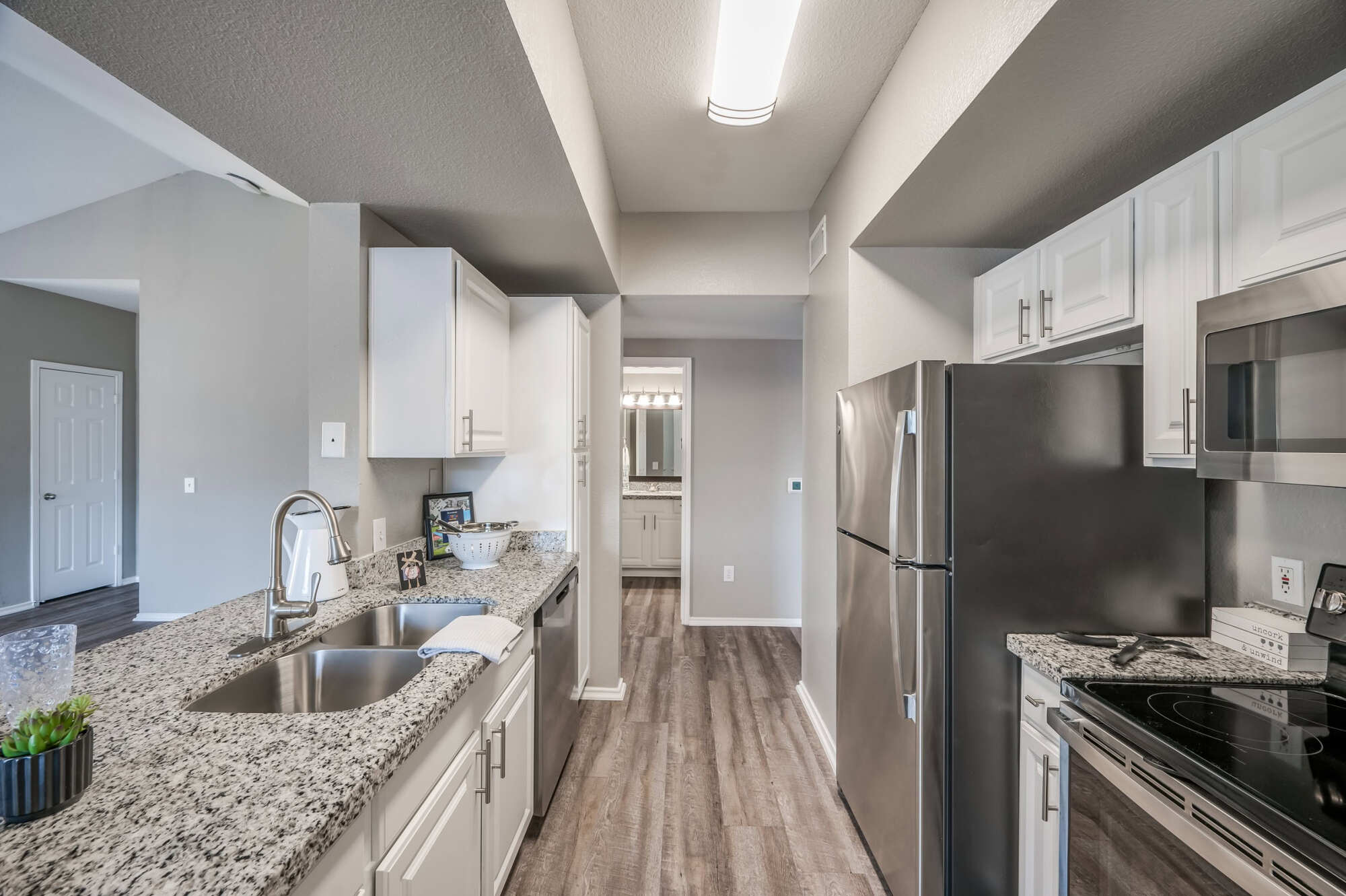 Apartment kitchen with white cabinetry, granite countertops, stainless steel refrigerator and microwave, and a breakfast bar opening to the dining area.