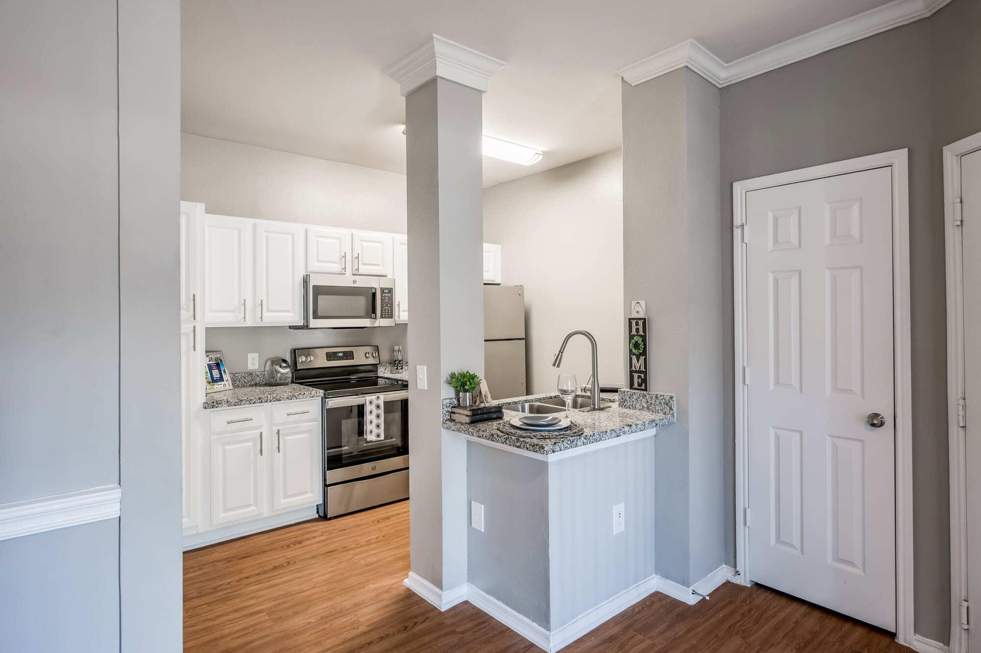 Apartment kitchen with white raised-panel cabinets, granite countertops, stainless steel appliances, and a peninsula breakfast bar, beside a white pantry door.