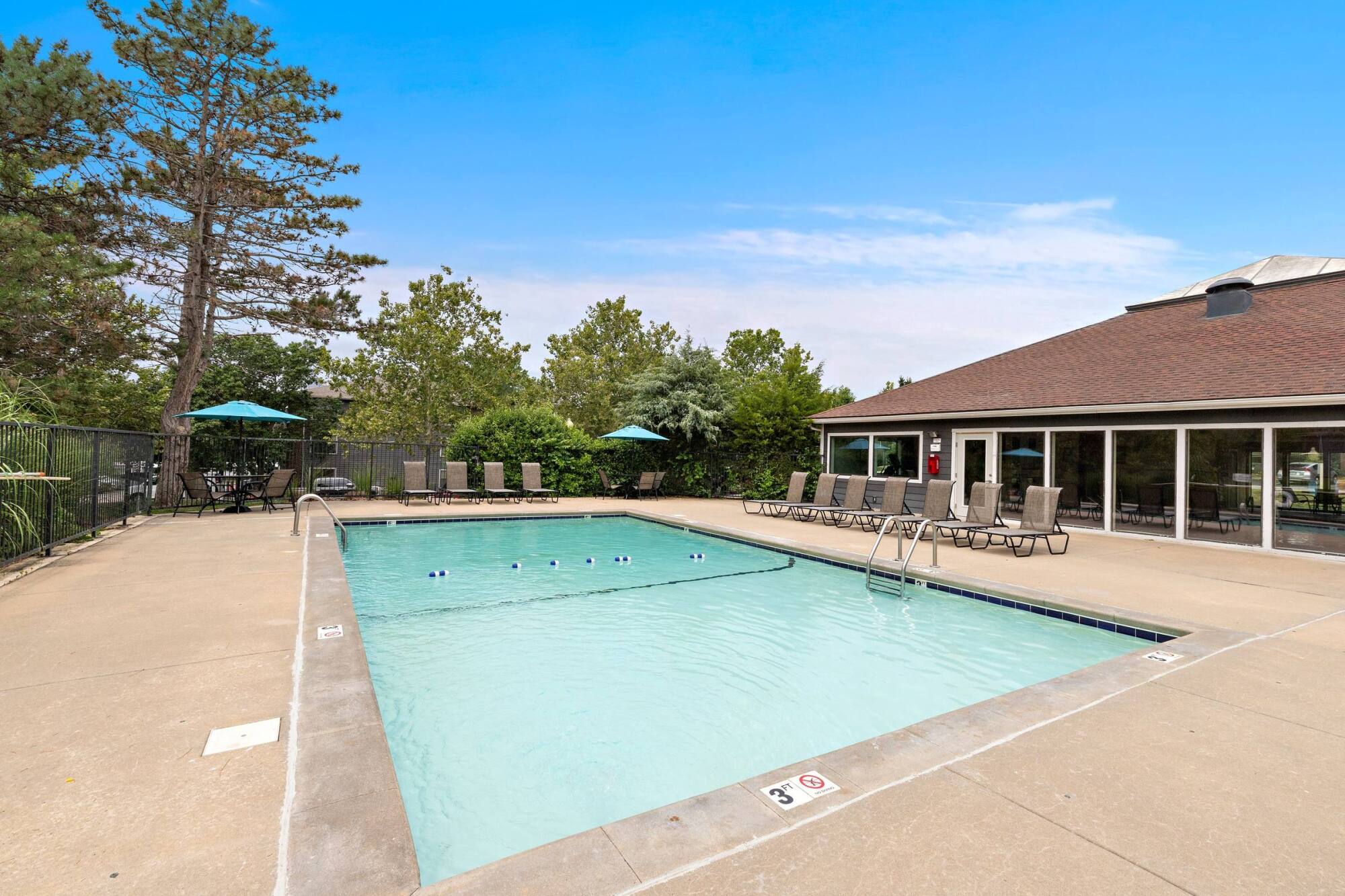 Sparkling outdoor pool at Timberlane Village Apartments in Kansas City, MO with poolside loungers and the clubhouse beyond.