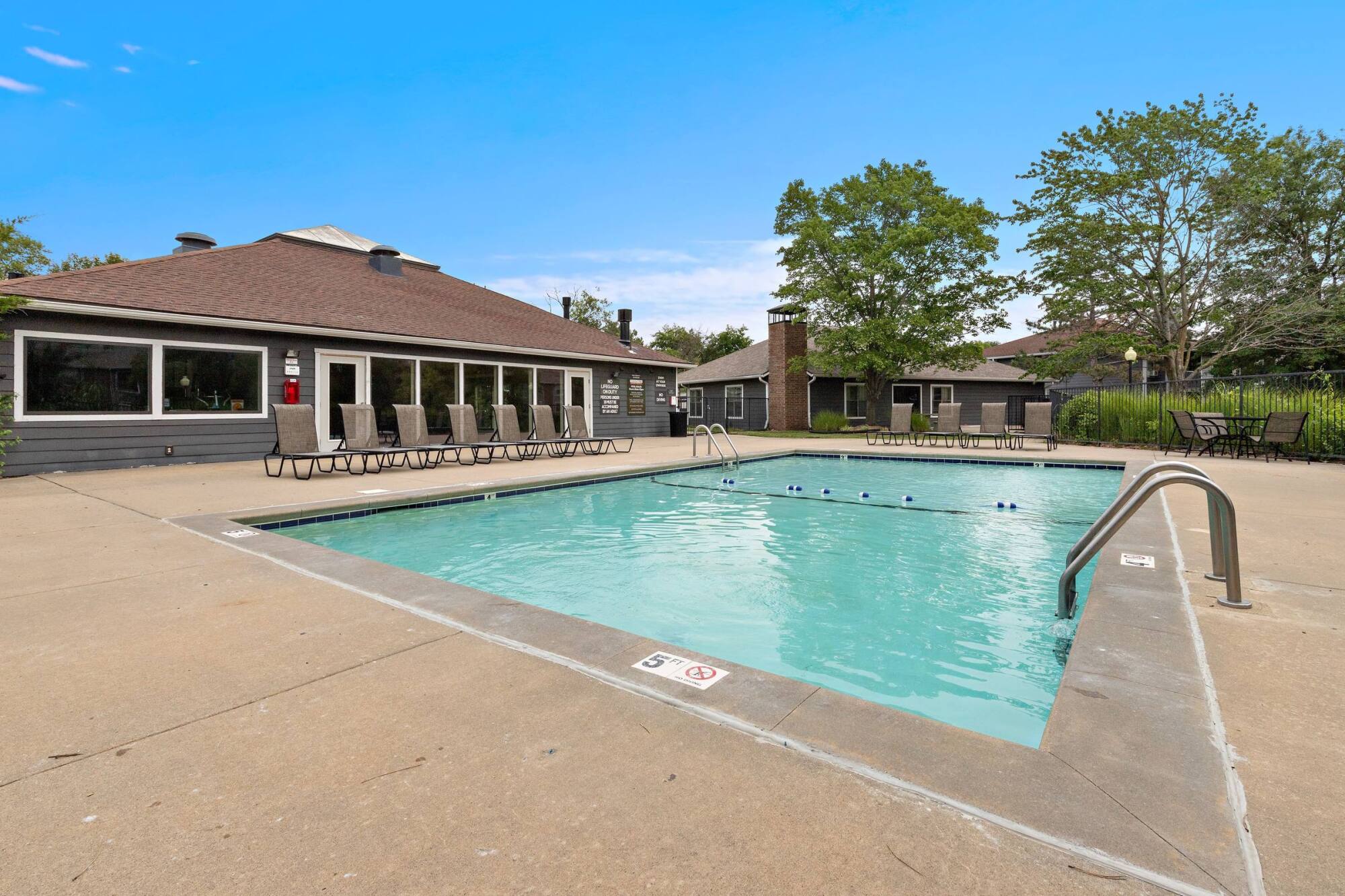 Outdoor pool and sundeck steps from the Timberlane Village clubhouse in Kansas City, MO, lined with lounge chairs.