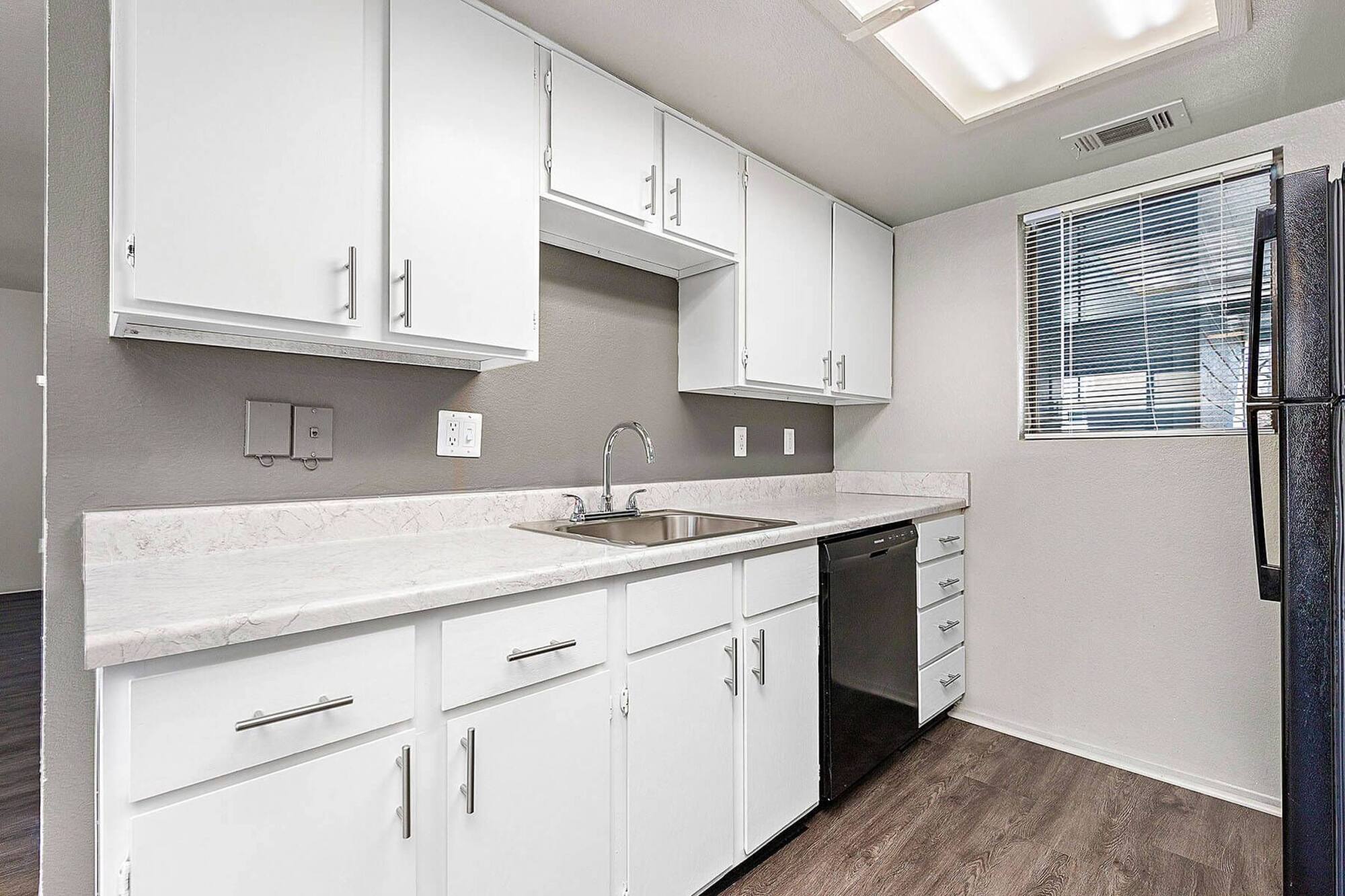 Galley kitchen at Timberlane Village with white cabinetry, marble-look counters, a gooseneck faucet, and a black dishwasher.