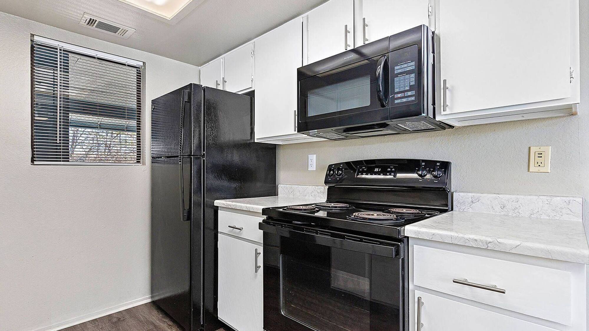 Timberlane Village kitchen with black appliances, an over-range microwave, white cabinets, and marble-look countertops.