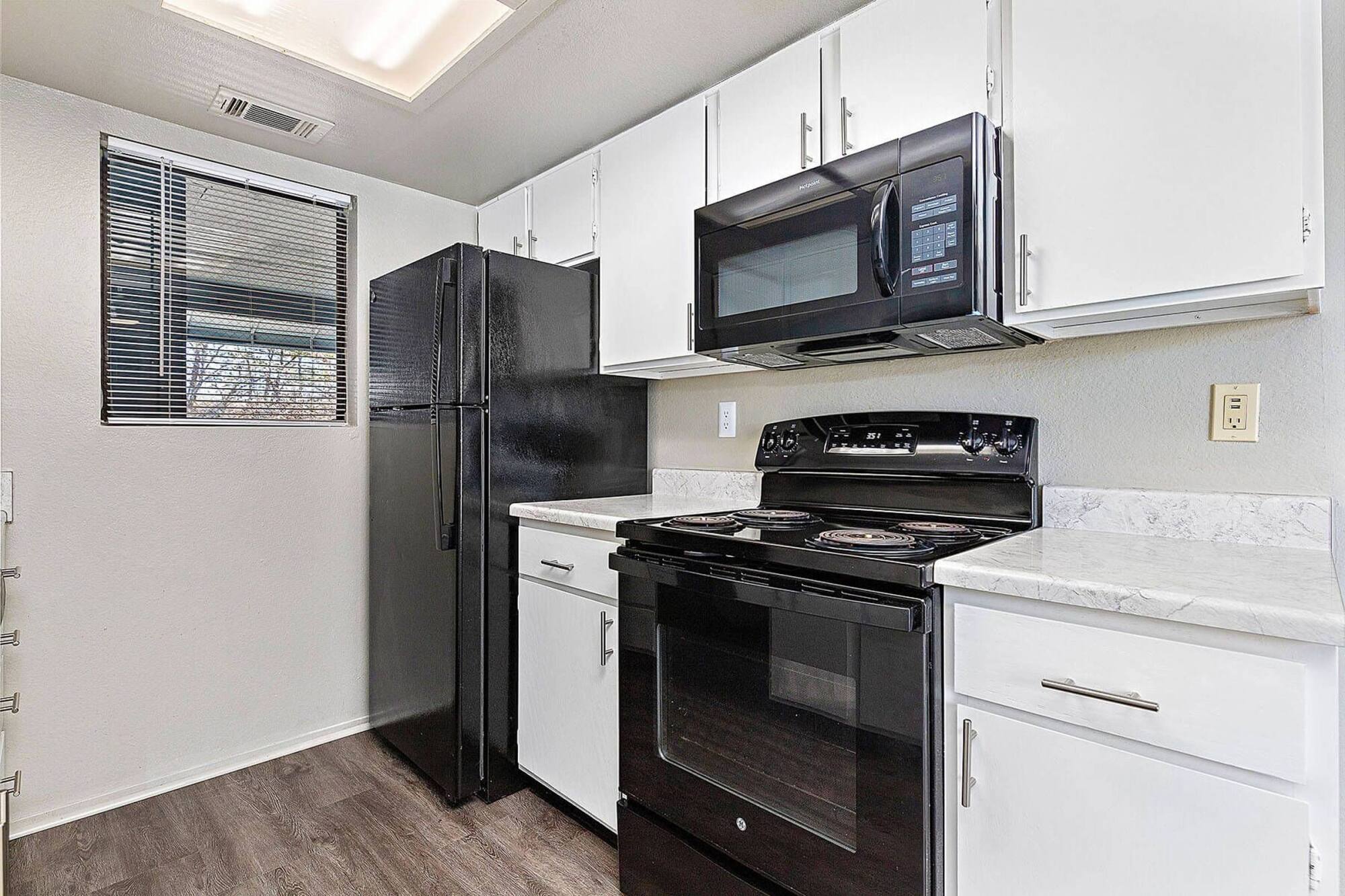 Timberlane Village apartment kitchen with a black refrigerator, electric range, and over-range microwave beneath white cabinetry.