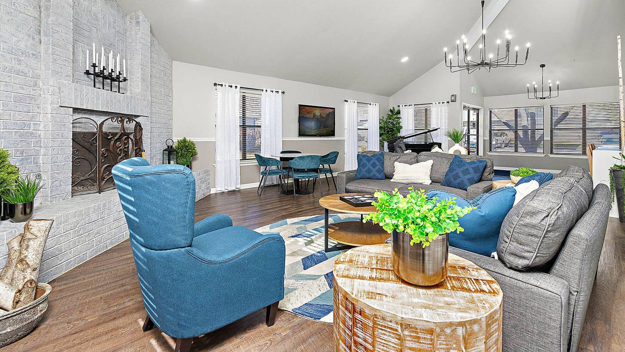 Clubhouse lounge at Timberlane Village Apartments in Kansas City, MO with blue armchairs, a brick fireplace, and a grand piano.