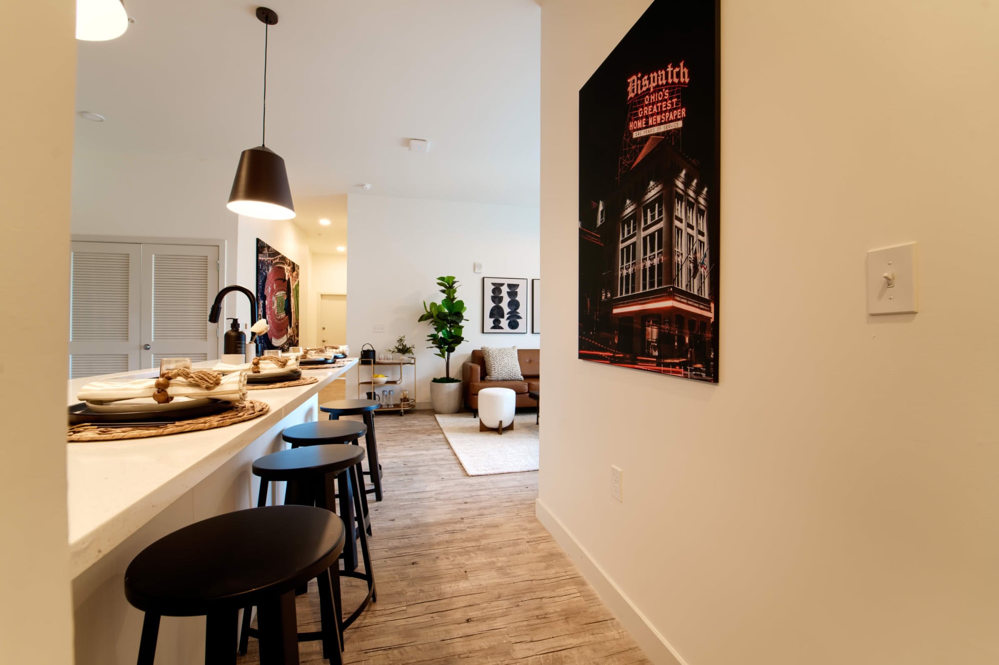 View past a kitchen peninsula with place settings toward a living room, with a framed "Dispatch" Columbus newspaper photo on the wall.